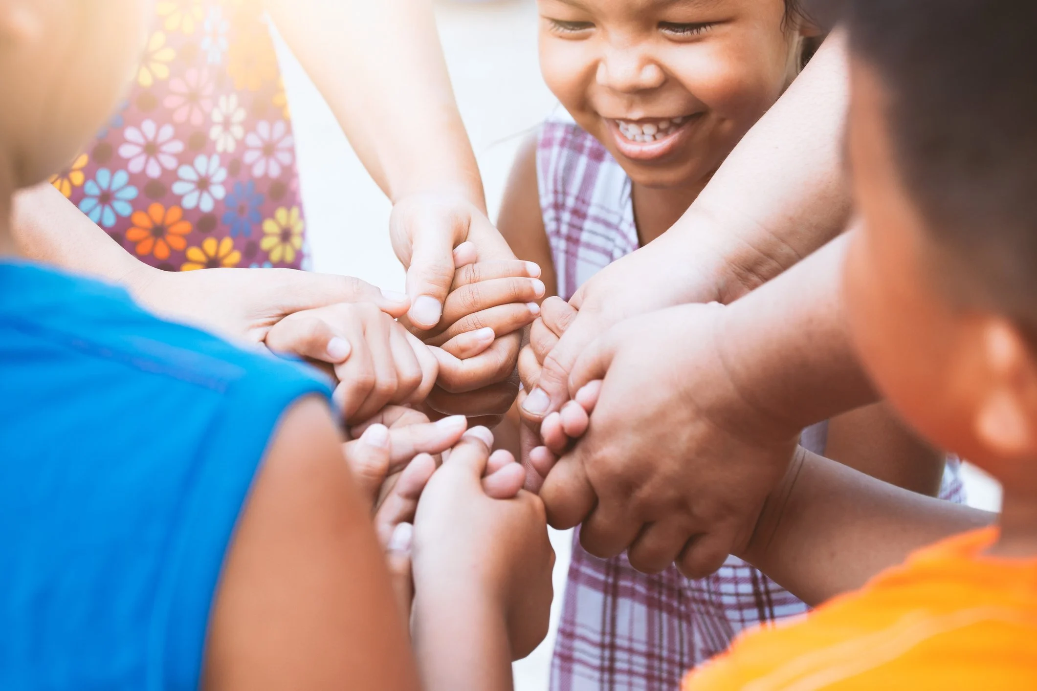 Children and adults' hands stacked together in the center, smiling faces surrounding the hands.