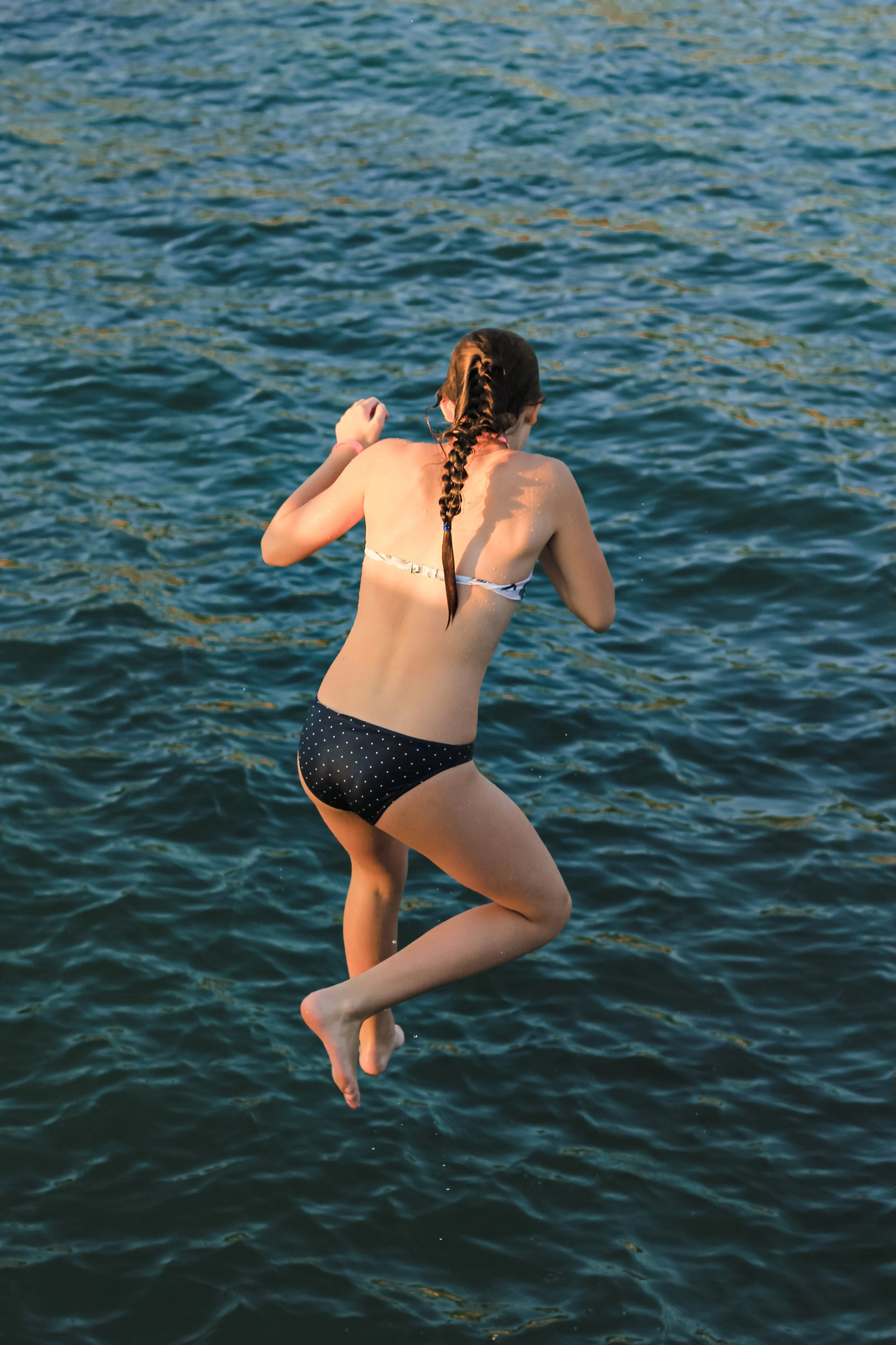 Jeune fille sautant dans l'eau à la mer ou un lac, vue de dos, avec un maillot de bain à pois