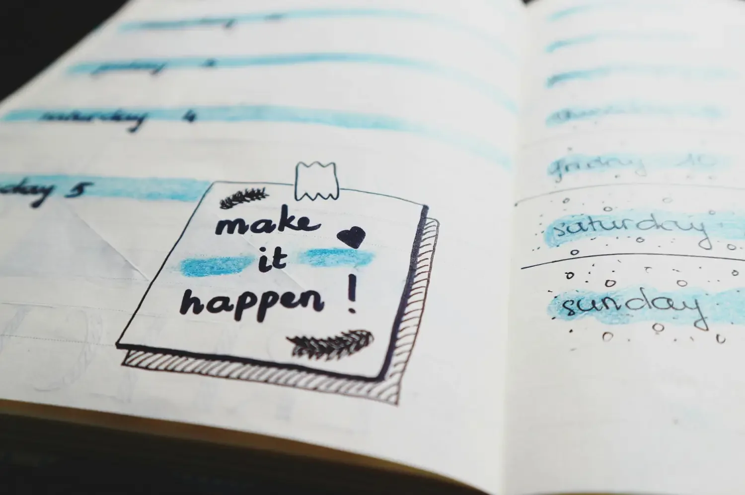 A journal page with handwritten notes and a small illustration of a notebook with the words 'make it happen!' in black ink, adorned with a small heart and decorative elements. Some words are highlighted with blue and the days of the week are written with blue highlight.