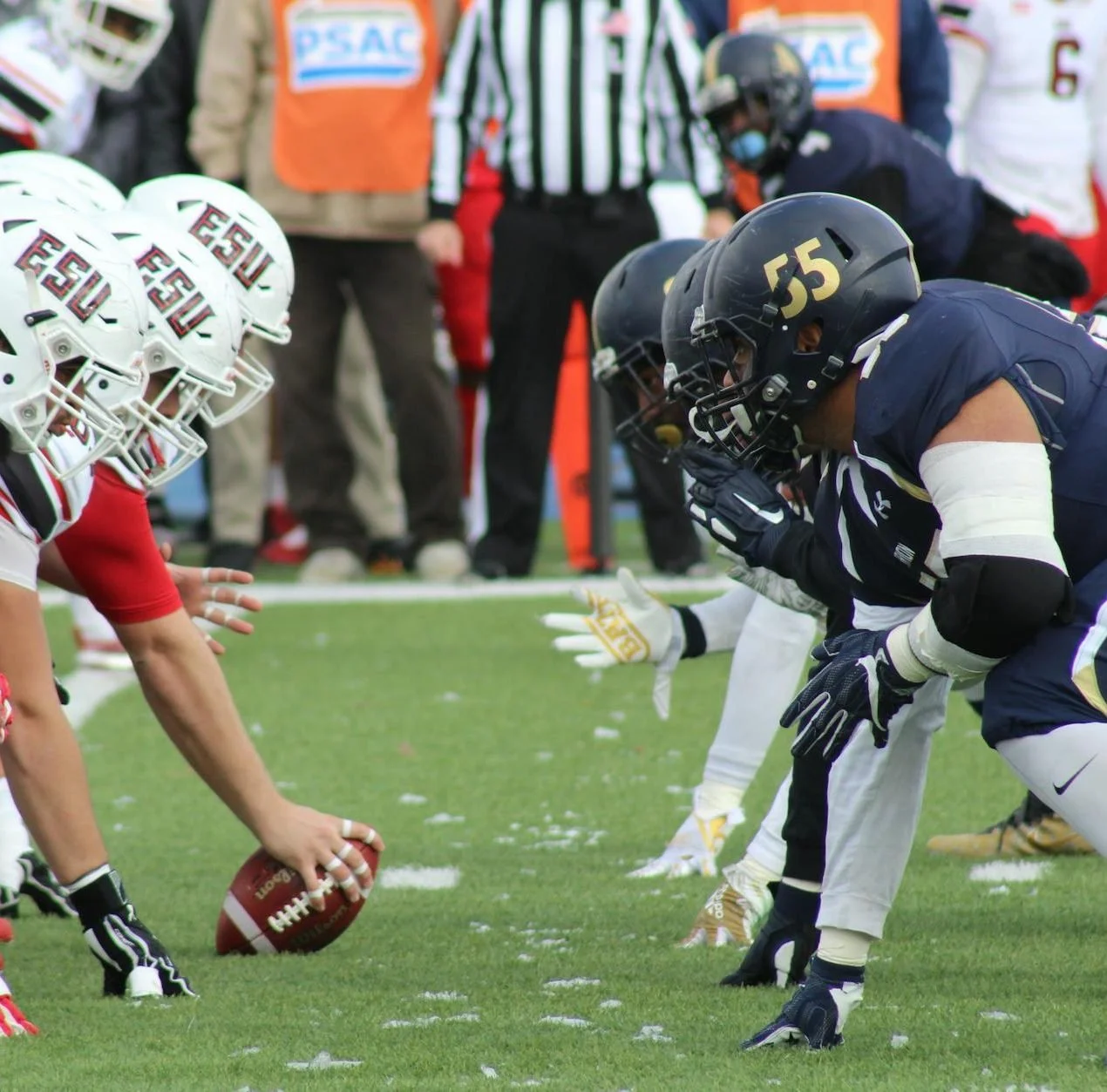 American football players lined up at the line of scrimmage during a game, with a referee in the background.