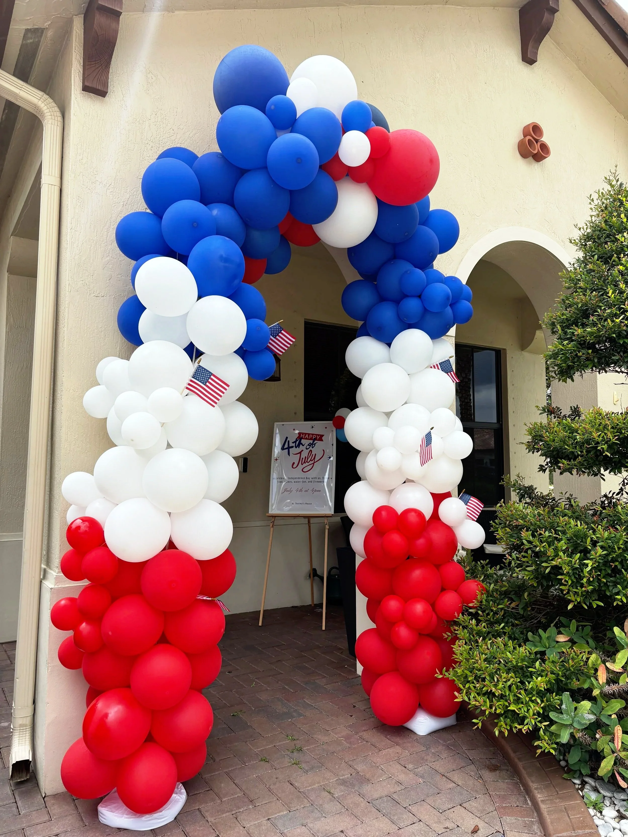 Red, white, and blue balloon arch decorated with small American flags, celebrating the 4th of July.