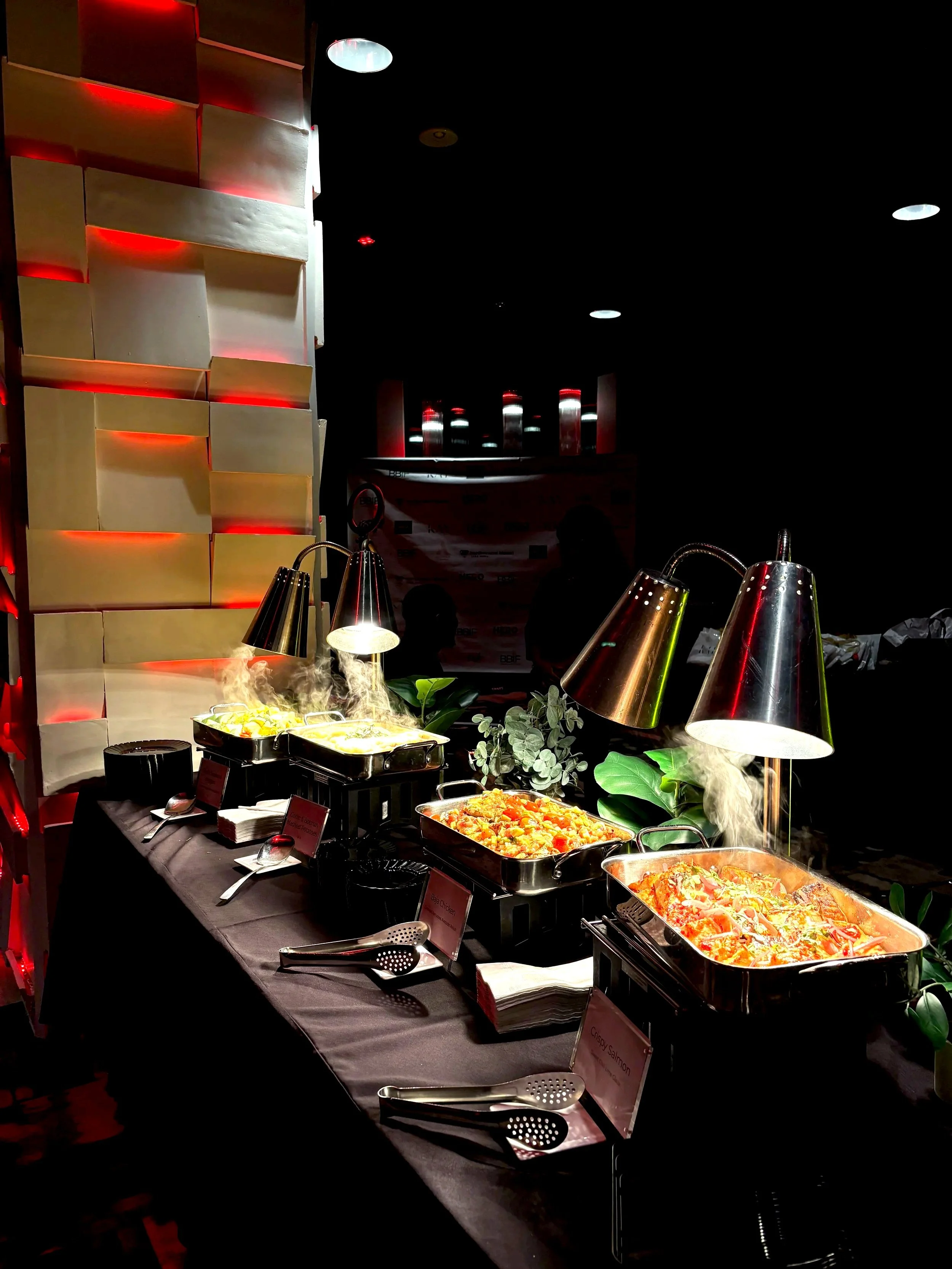 Long outdoor dining table with floral arrangements, candles, and string lights in a garden setting.