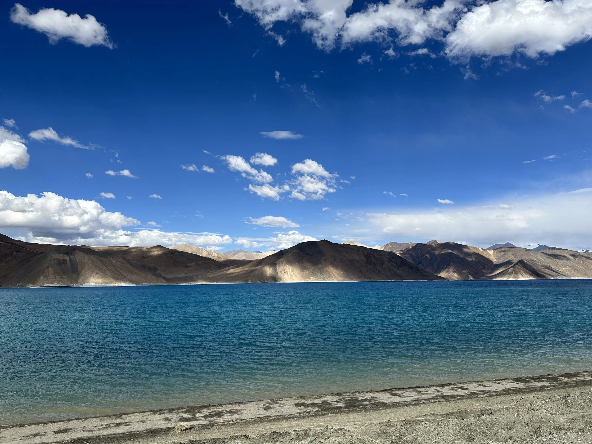 Scenic view of a large blue lake with mountains in the background and a partly cloudy sky overhead.