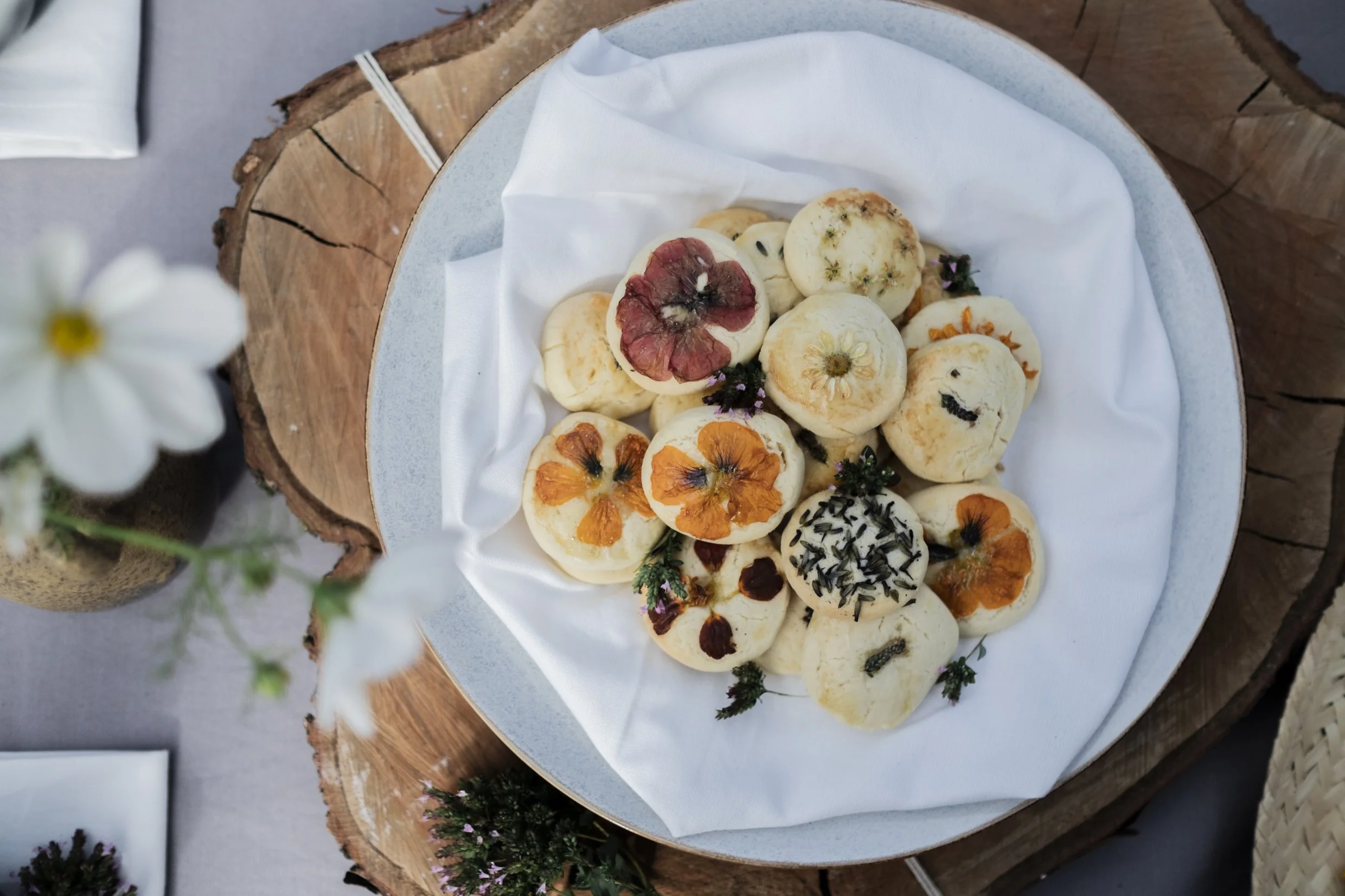 Selbstgemachte Muffins mit essbaren Blumen, auf einer weißen Serviette in einer großen, hellen Schale, auf einem rustikalen Holzbrett, mit kleinen Blumen und Dekorationen