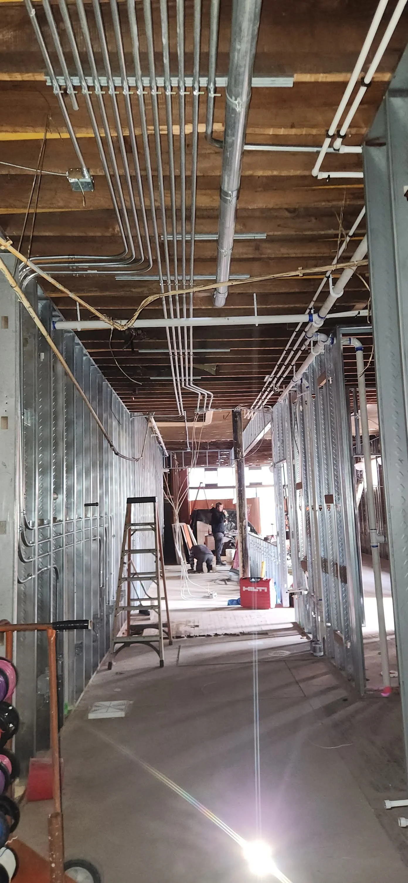 Construction site with electrical wiring and metal framing, workers in background, and a ladder.