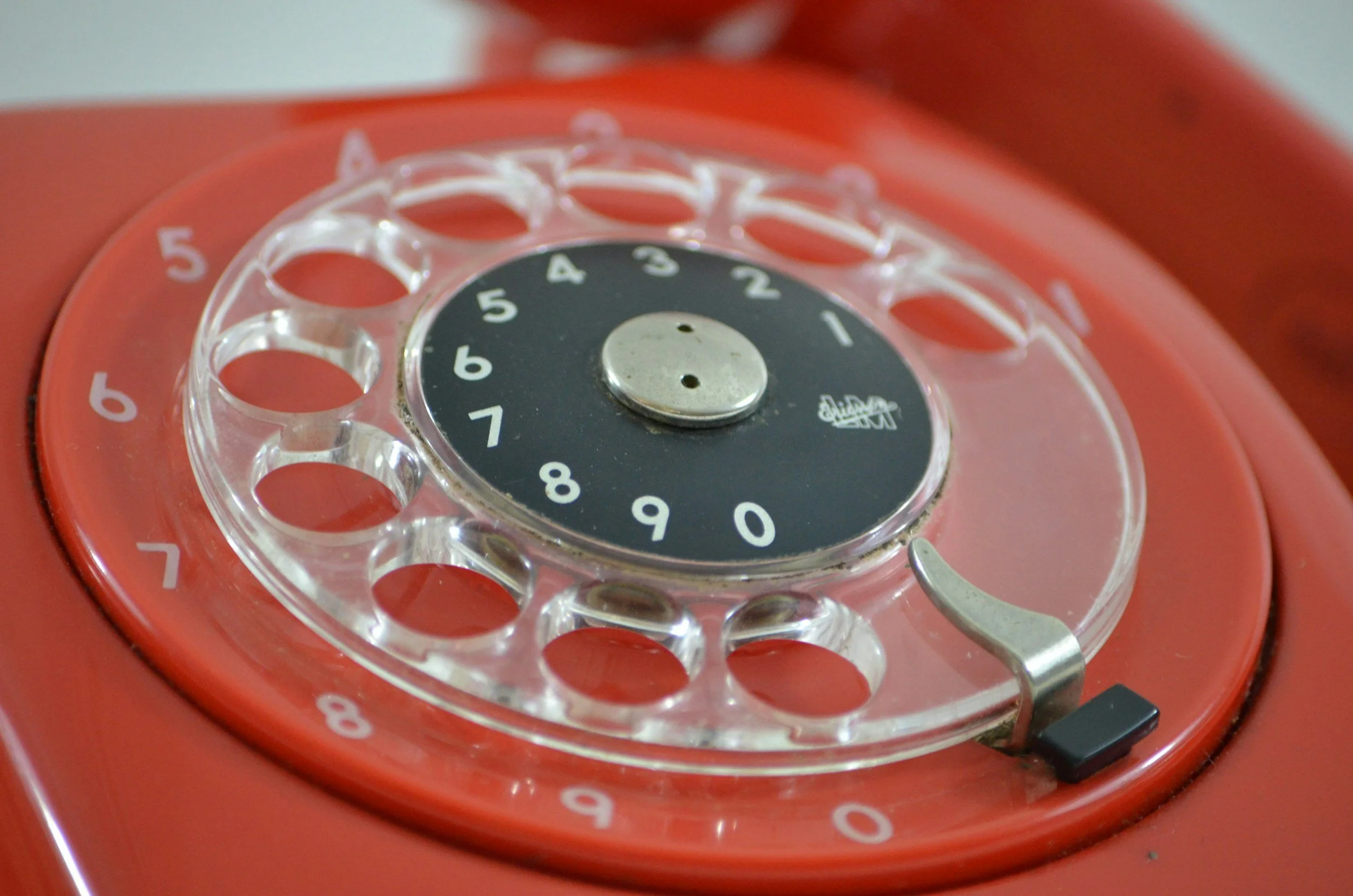 Close-up of a vintage red rotary telephone dial with a black center and white numbered ring.