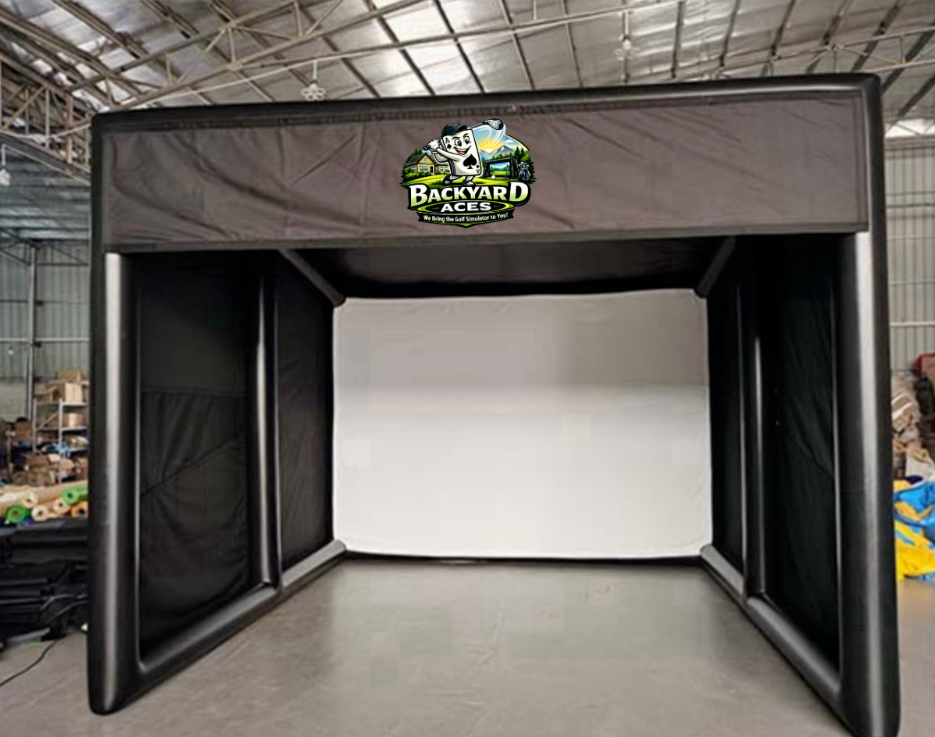 Indoor golf simulator with a black frame and white projection screen, branded with Backyard Aces logo, in a warehouse setting.