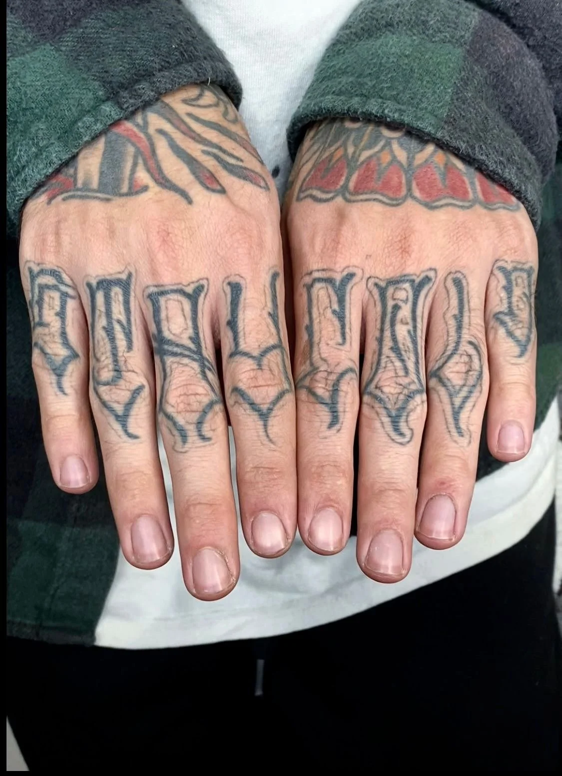 A pair of tattoos on the knuckles of two hands. The tattoos are bold, black-lettered words with decorative flames or flames surrounding the letters.