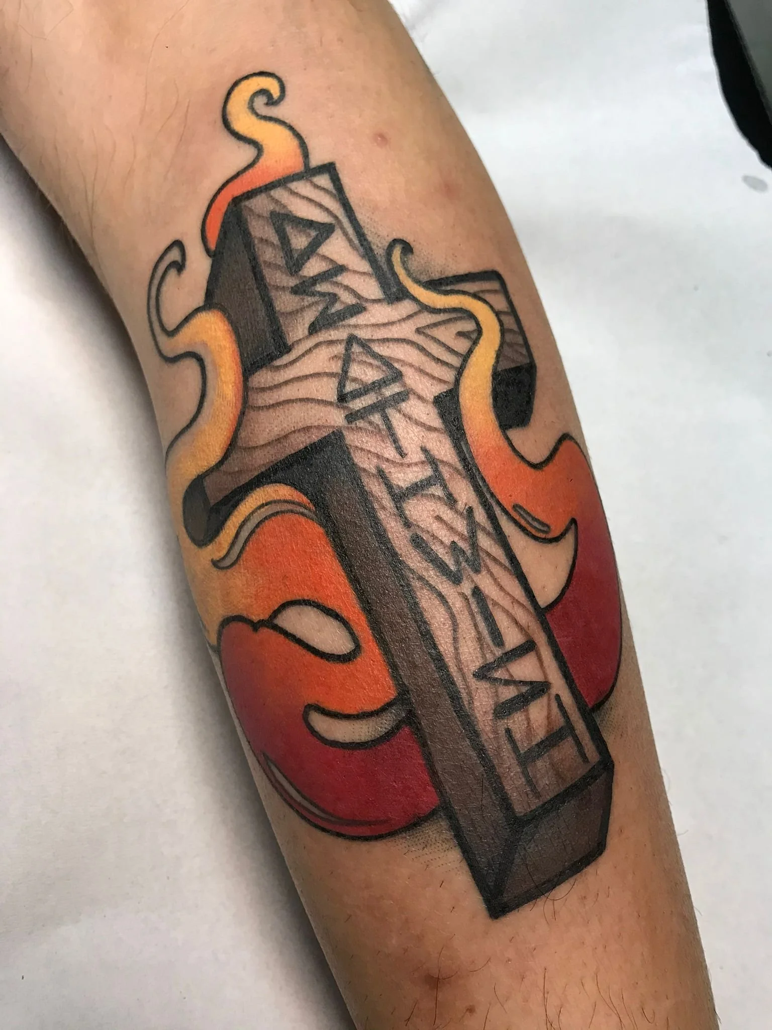 Tattoo of a wooden cross with the word 'faith' on it, surrounded by flames with red, orange, and yellow colors.