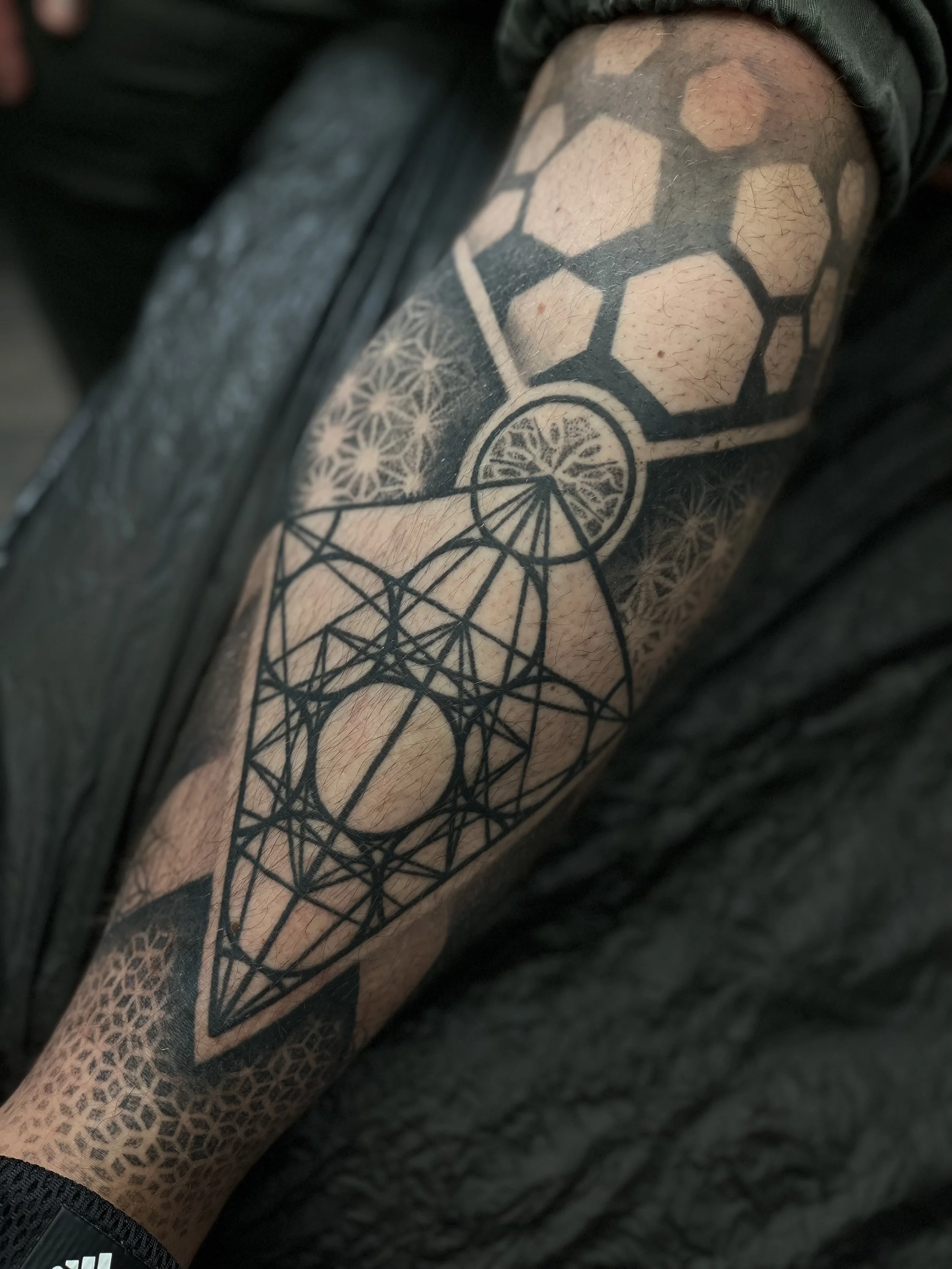 Tattoo on forearm featuring geometric patterns, hexagons, circles, and intricate lines.