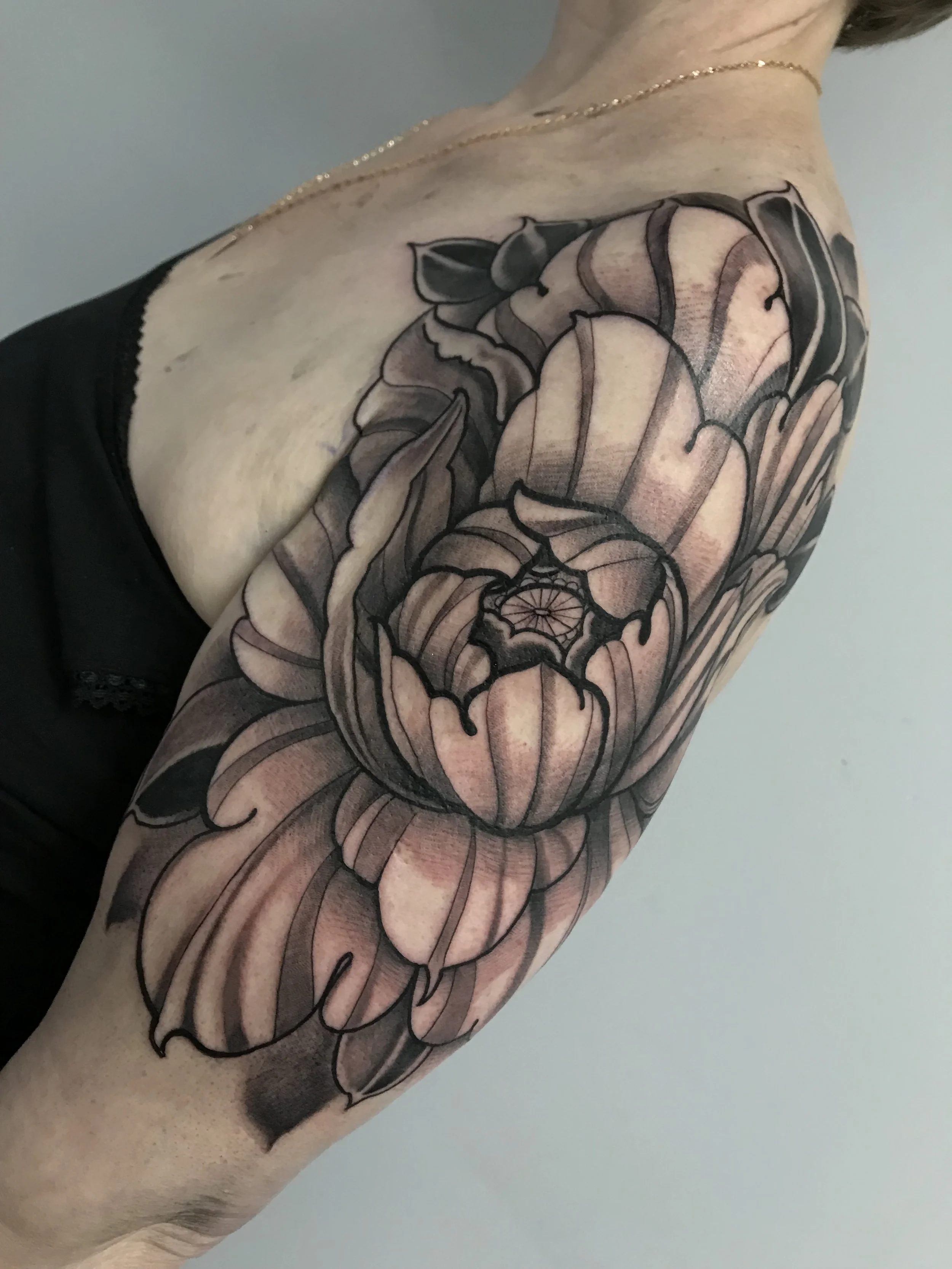 Black and gray floral tattoo on person's arm, featuring large tulip-like flowers with detailed shading and line work.