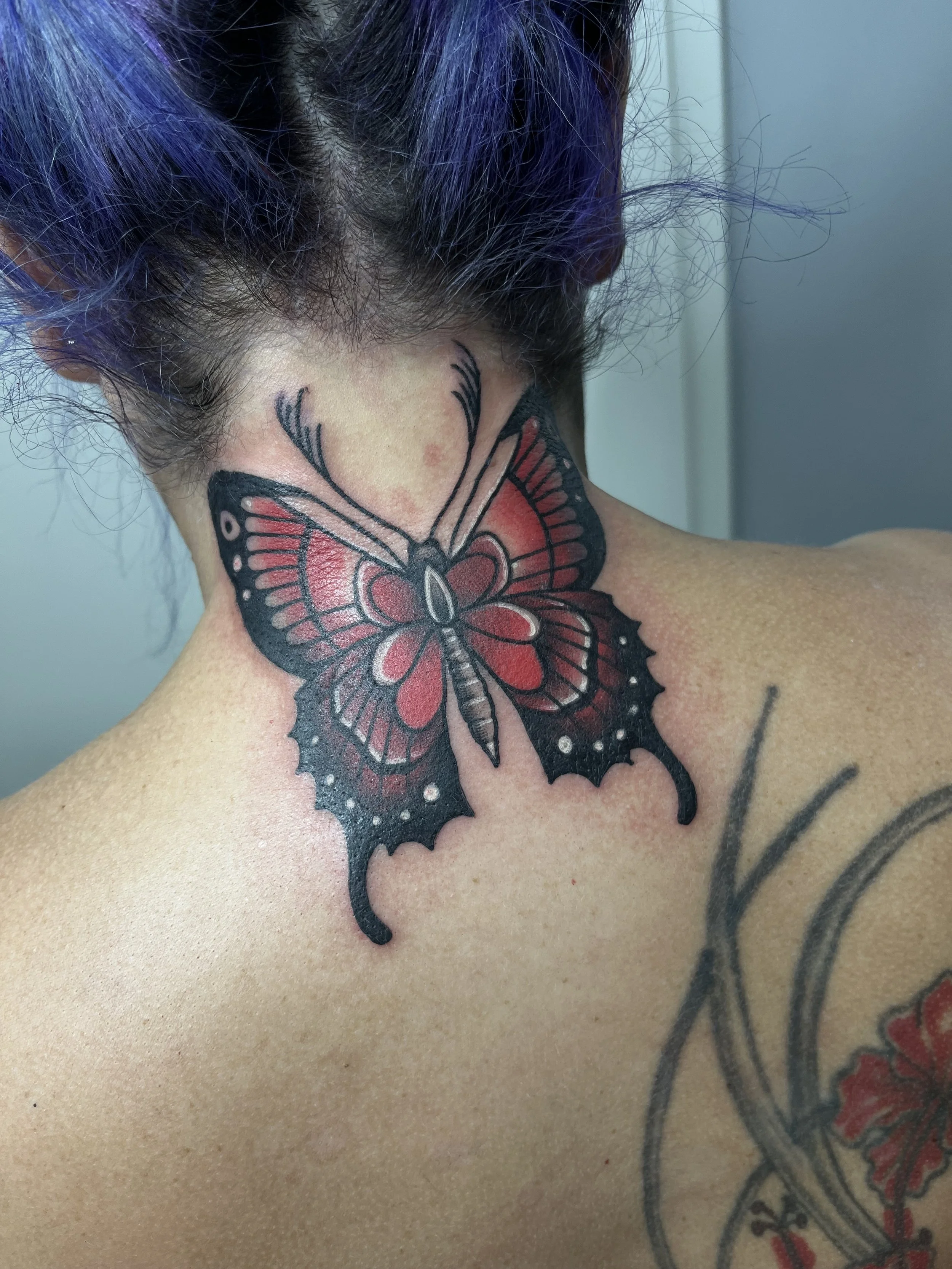 Tattoo of a red and black butterfly on the person’s neck.