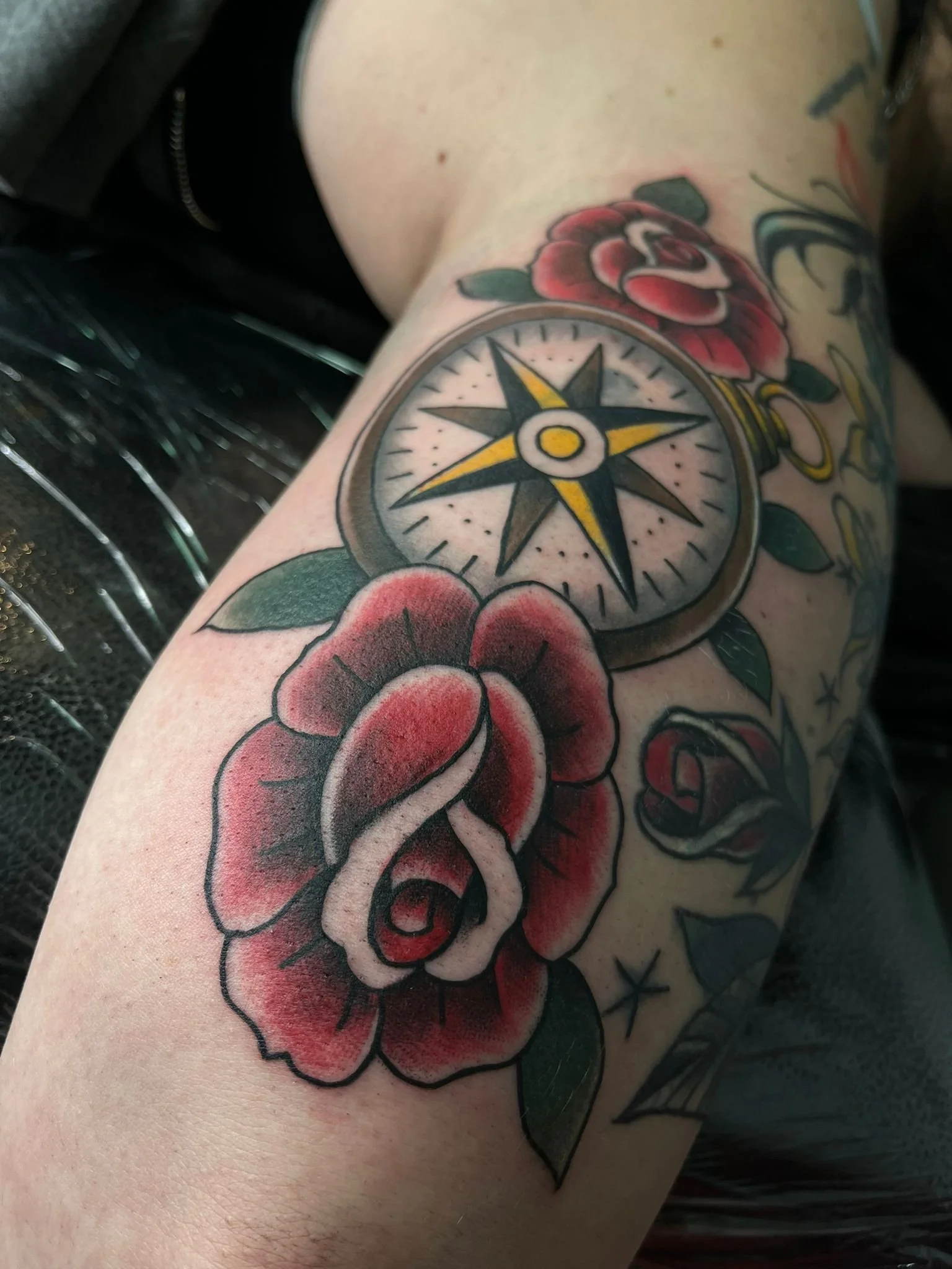 A tattoo of a compass surrounded by red roses with green leaves on a person's arm.