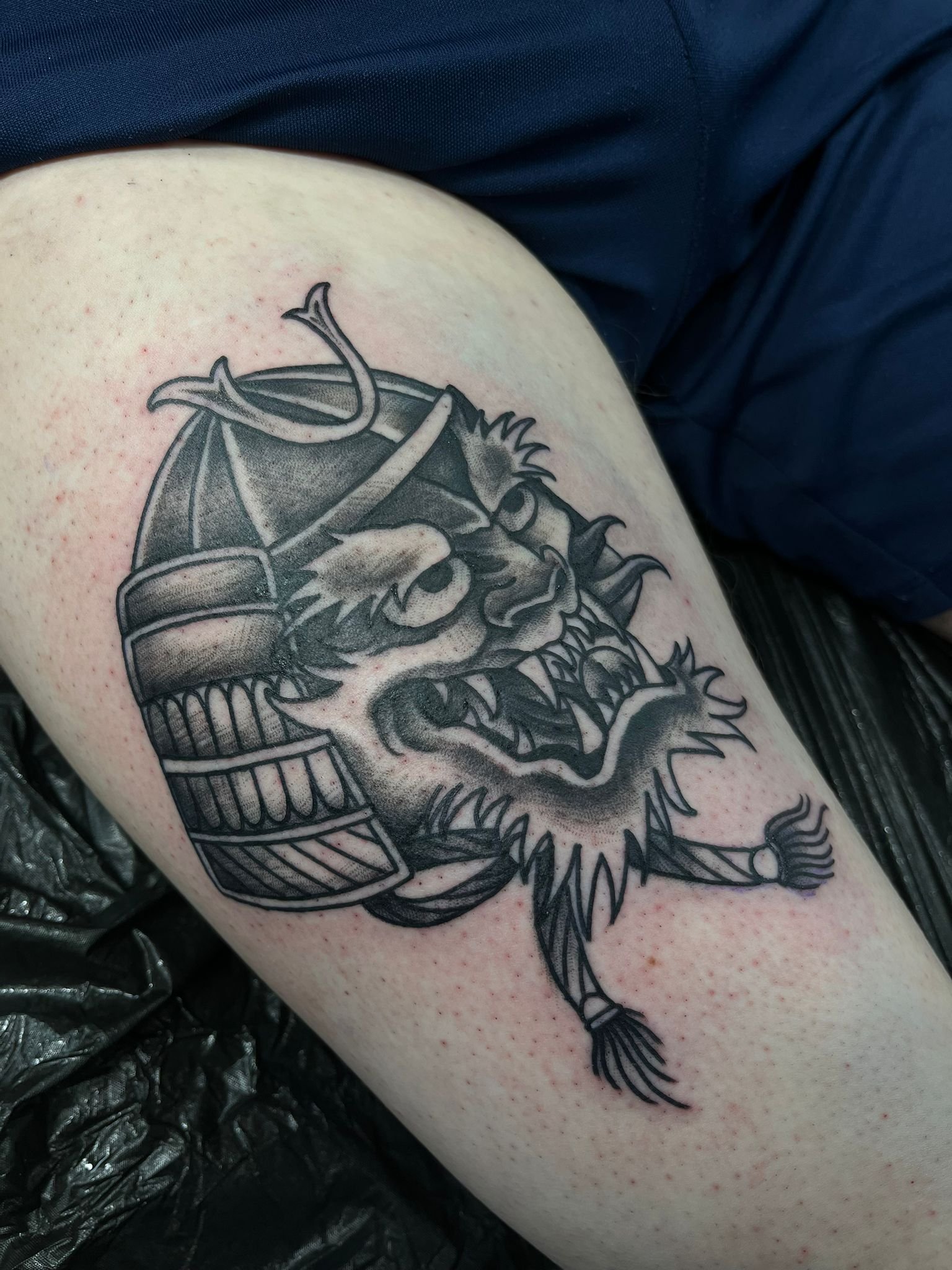 Black and gray tattoo of a fierce dragon's head wearing a samurai helmet on upper arm