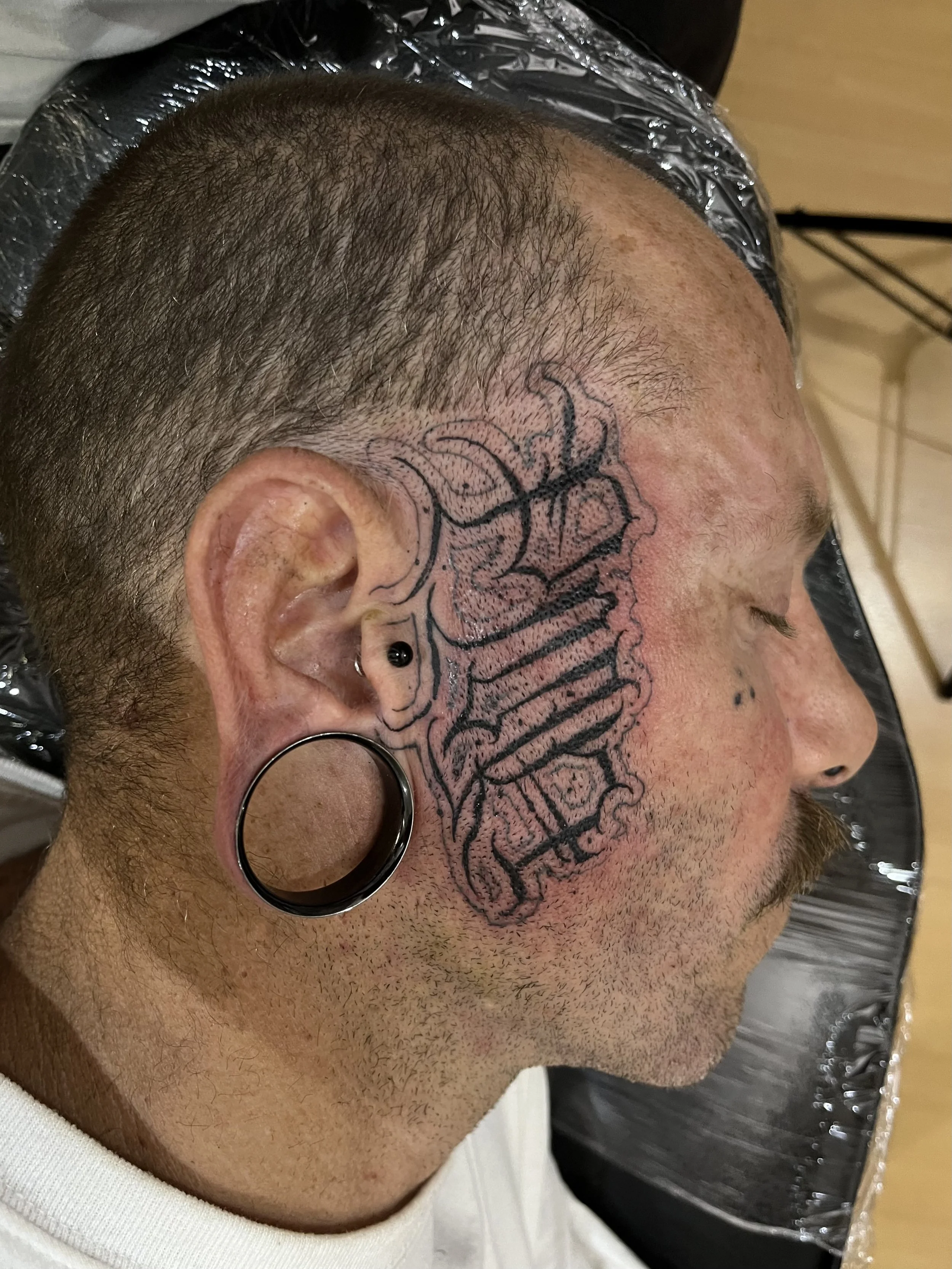 Dark Lettering Black and Grey PMA Face Tattoo Done By LonoTattoo