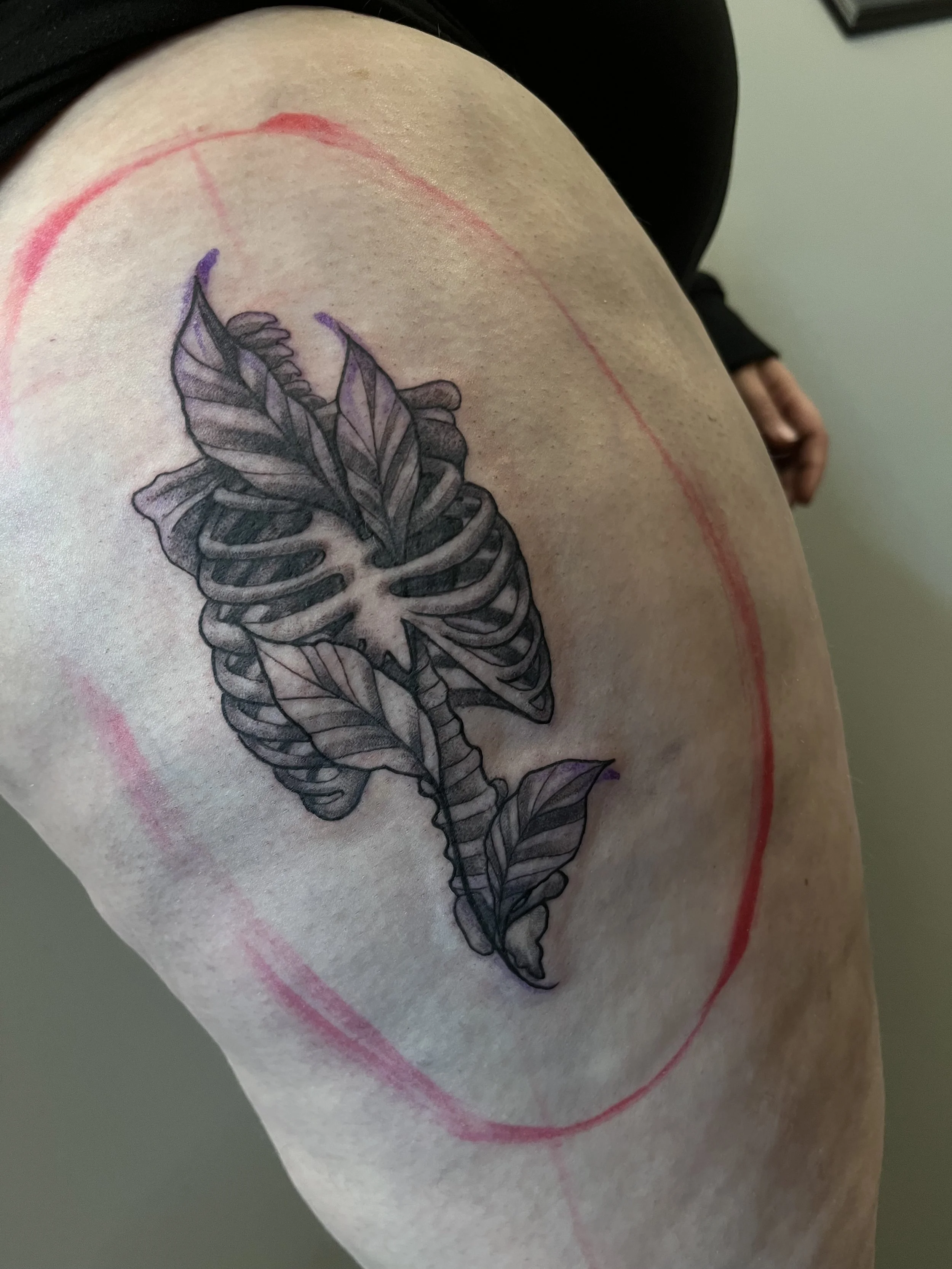 A tattoo of a butterfly with leaves on a person's upper arm, with red circle marks around it.