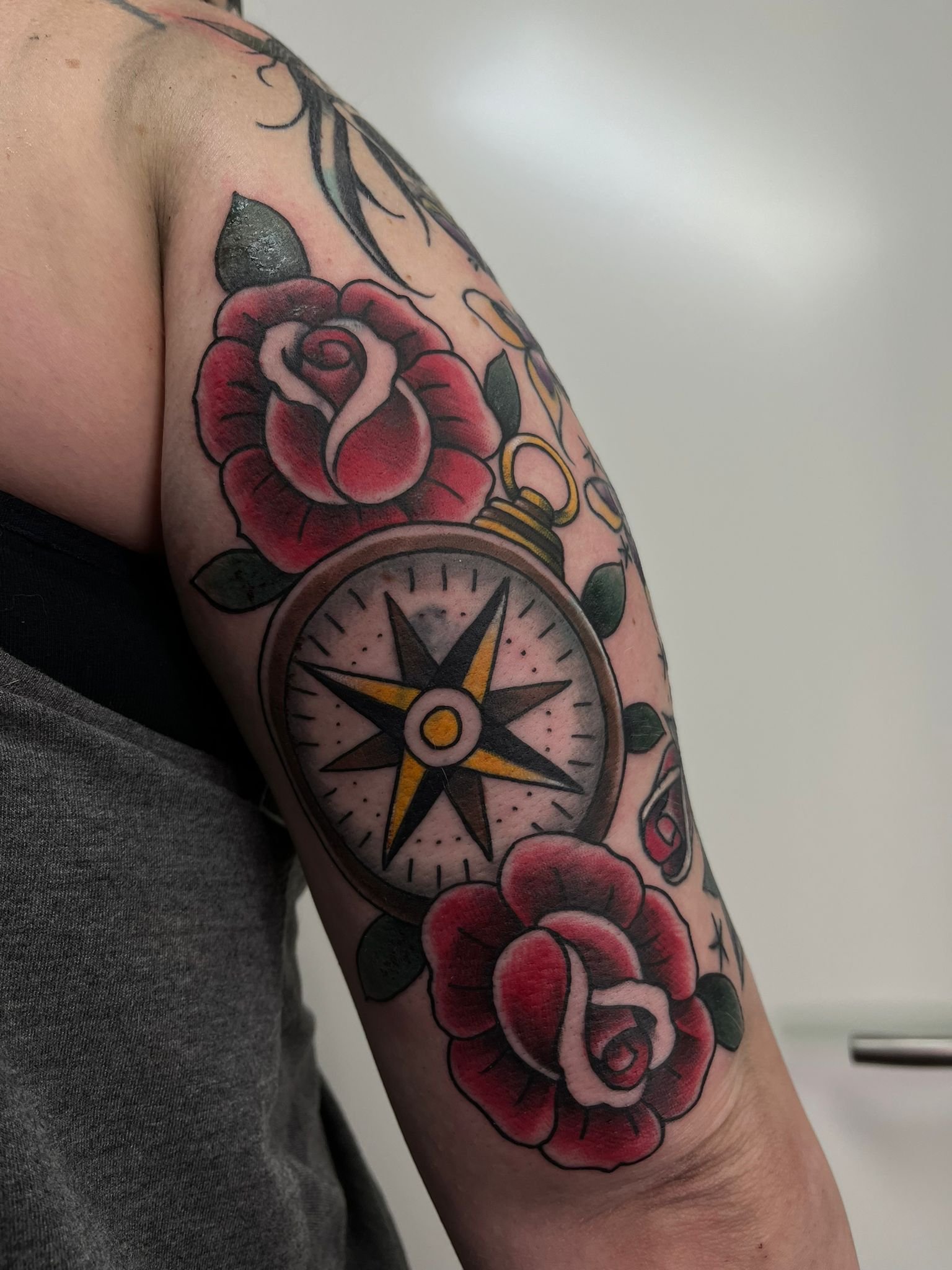 Tattoo of a pocket watch with roses and a small vial on the person's upper arm.