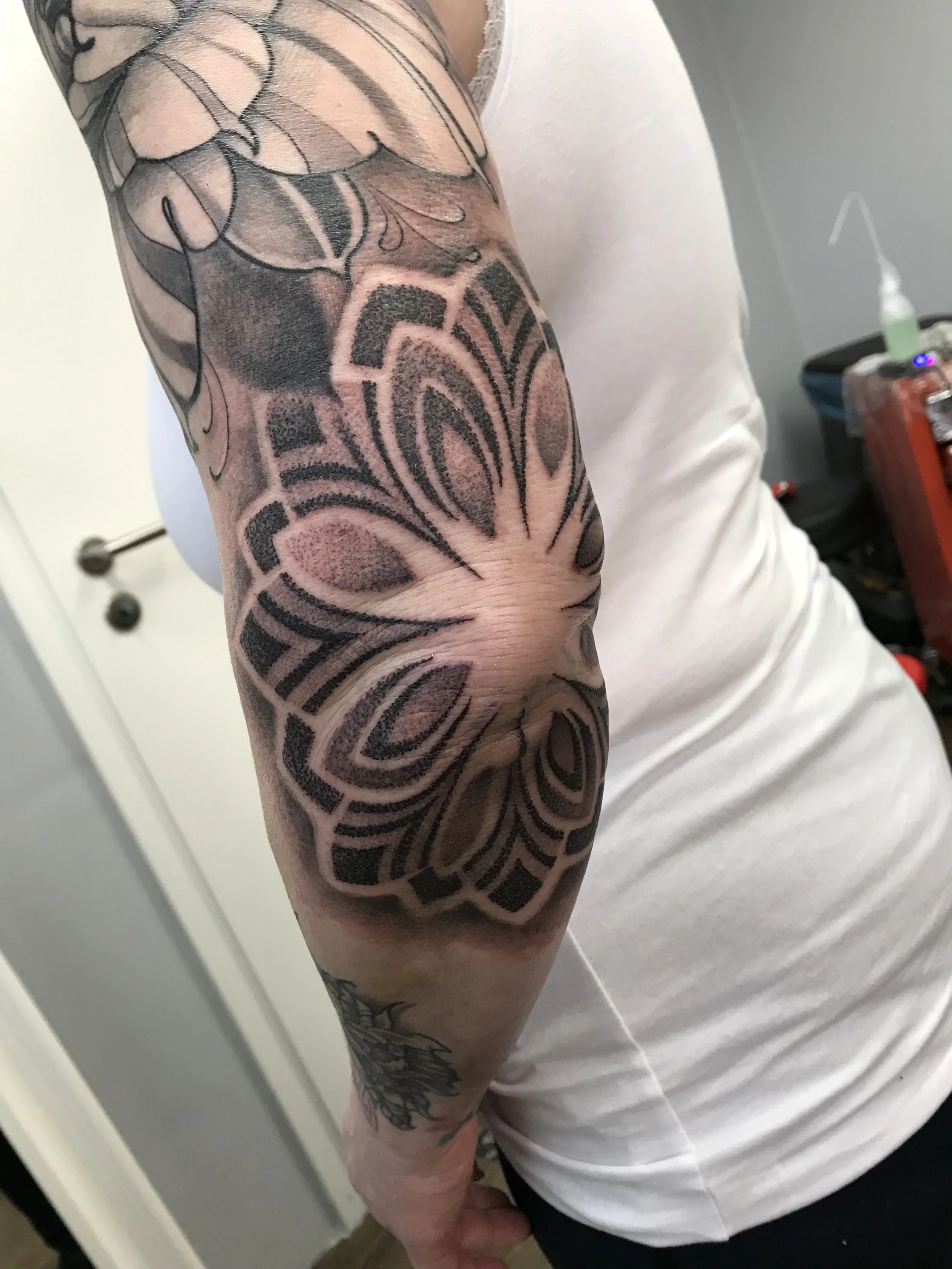 A person's upper arm with a large black and gray tattoo of a butterfly with intricate, stylized patterns