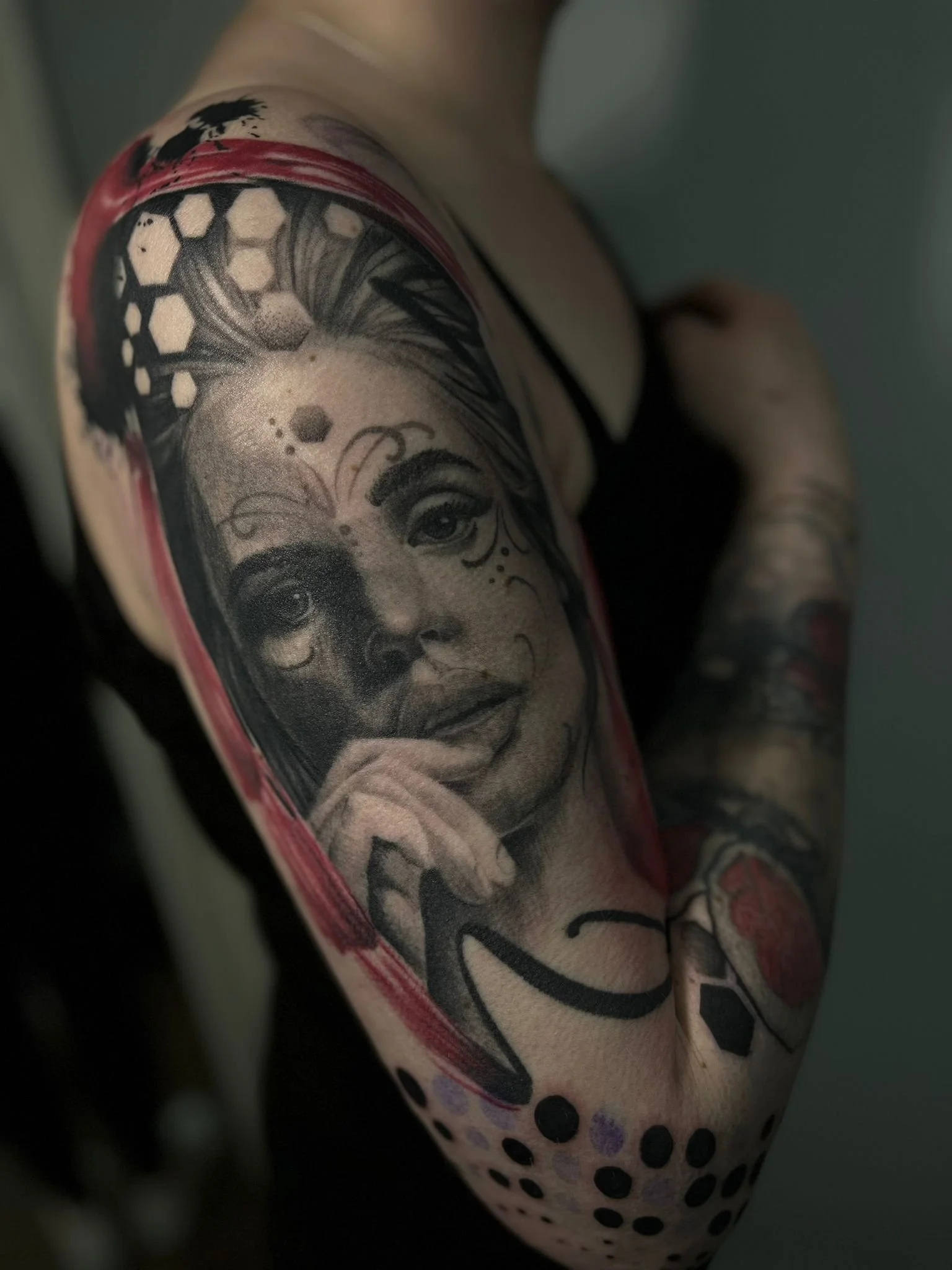 Close-up of a black and gray tattoo of a woman's face with a thoughtful expression on her chin on a person's upper arm.