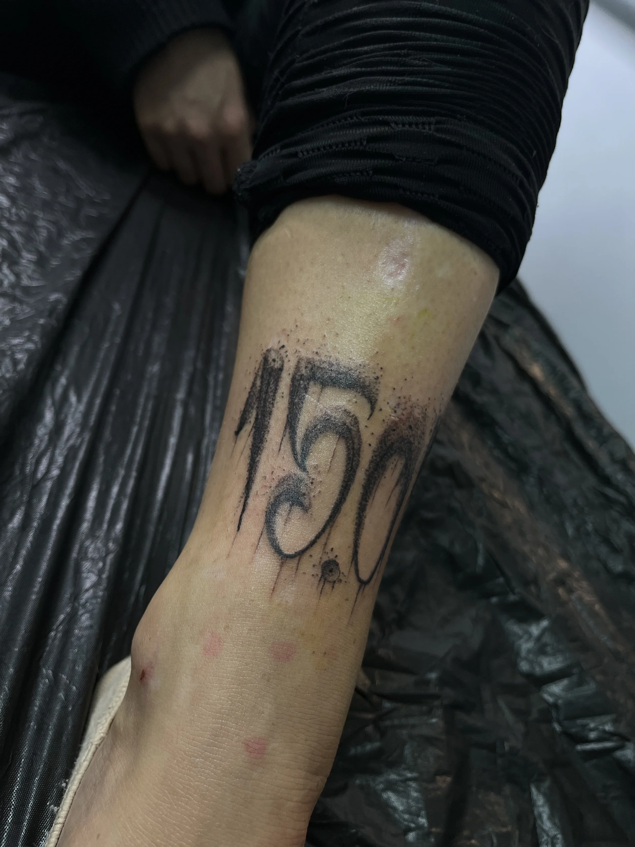 A tattoo of black, dripping-style numbers 16 on a person's forearm.