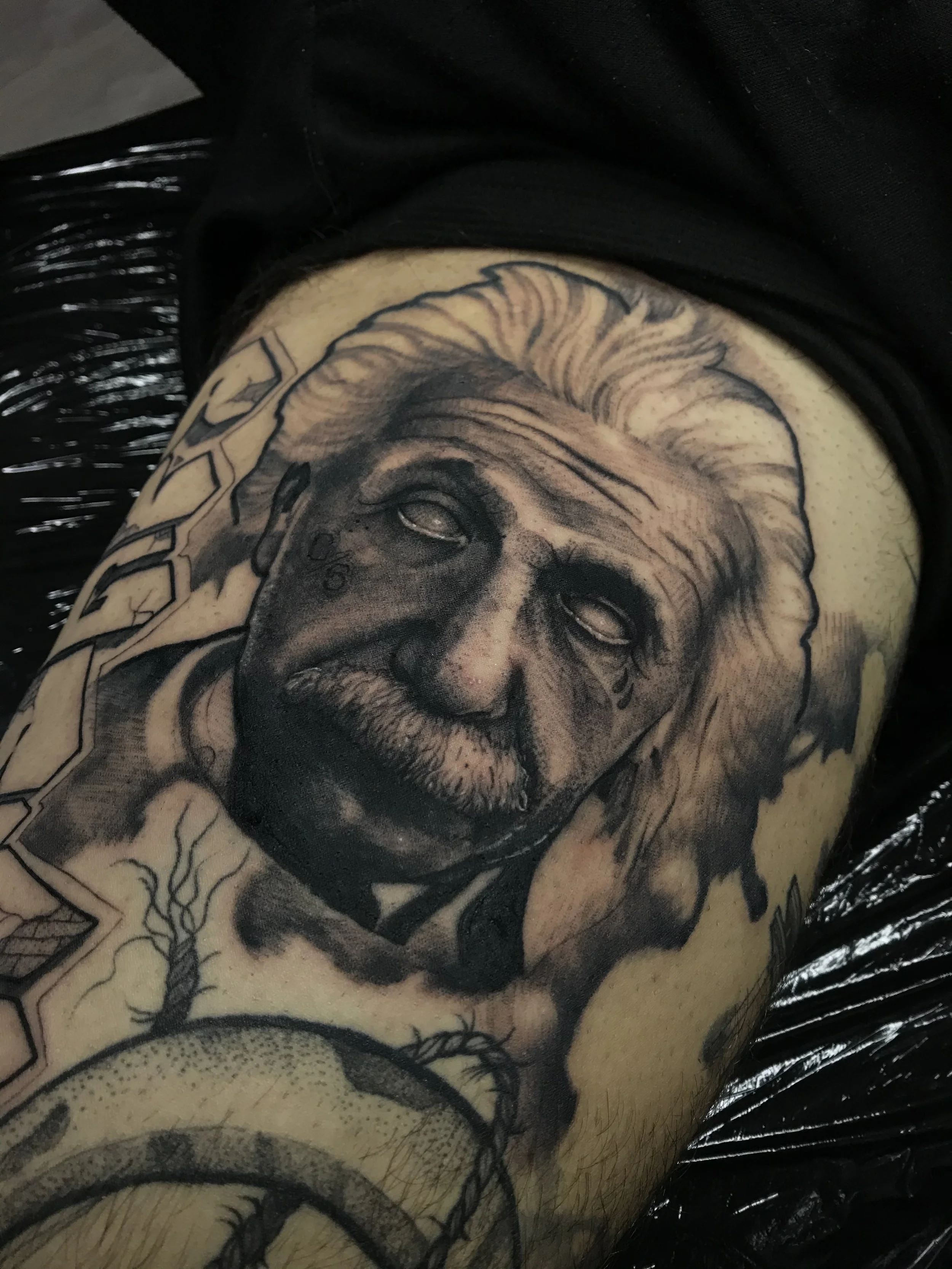 A detailed black and gray tattoo of Albert Einstein's face on a person's arm.