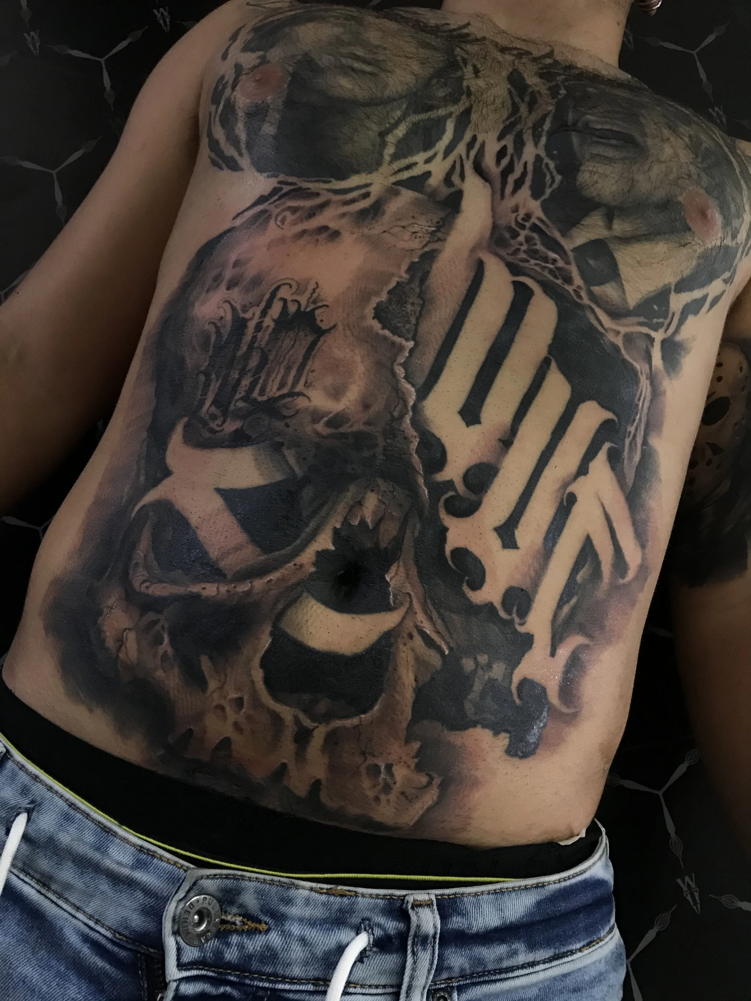 Close-up of a man's torso with a large tattoo featuring a skull, a clock, and Roman numerals.