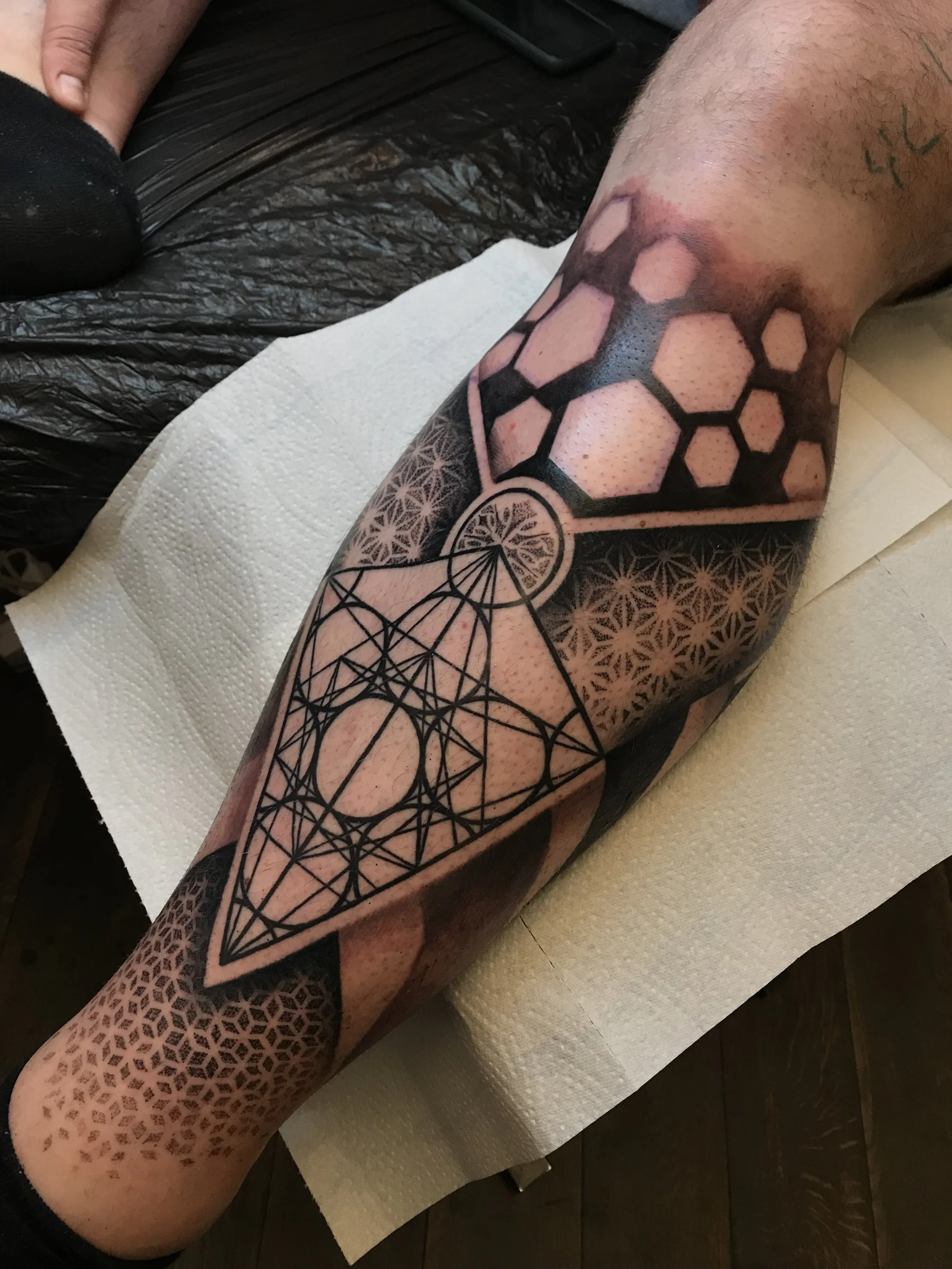 A person's forearm tattoo featuring geometric patterns, honeycomb designs, and interconnected circles with intricate line work.