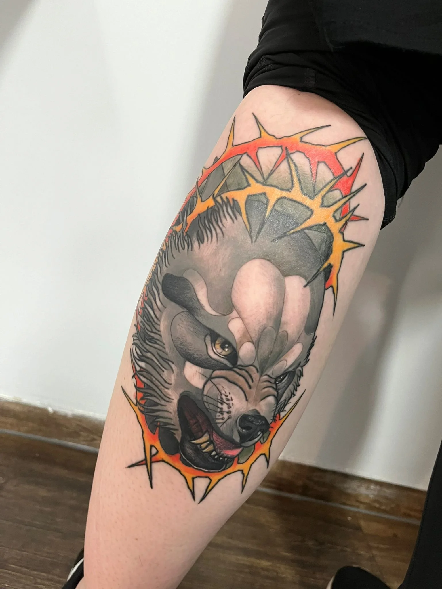 Tattoo of a snarling wolf's face with a fiery background on a person's thigh.