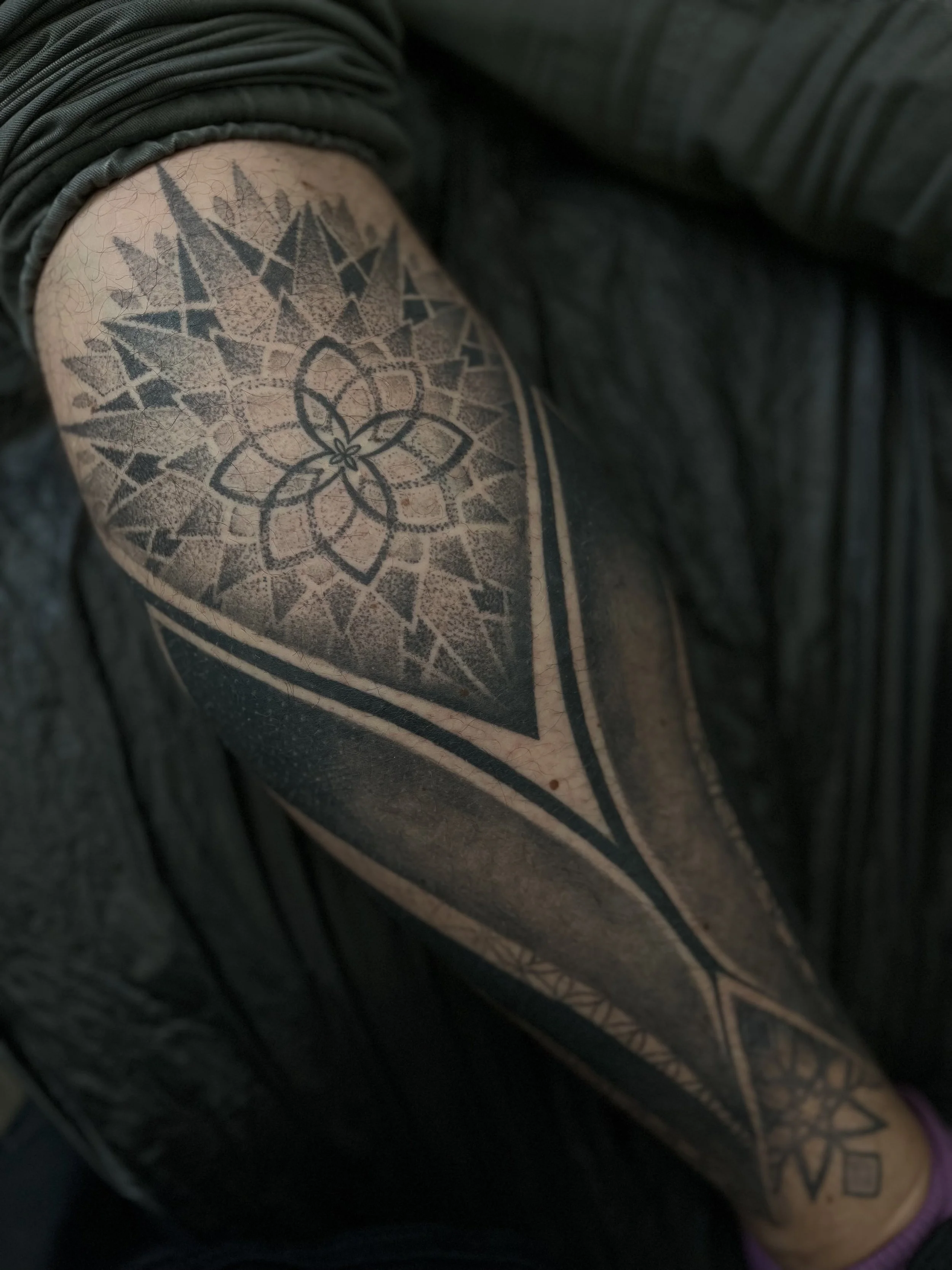 Close-up of a person's upper arm showing a black geometric and floral tattoo design.
