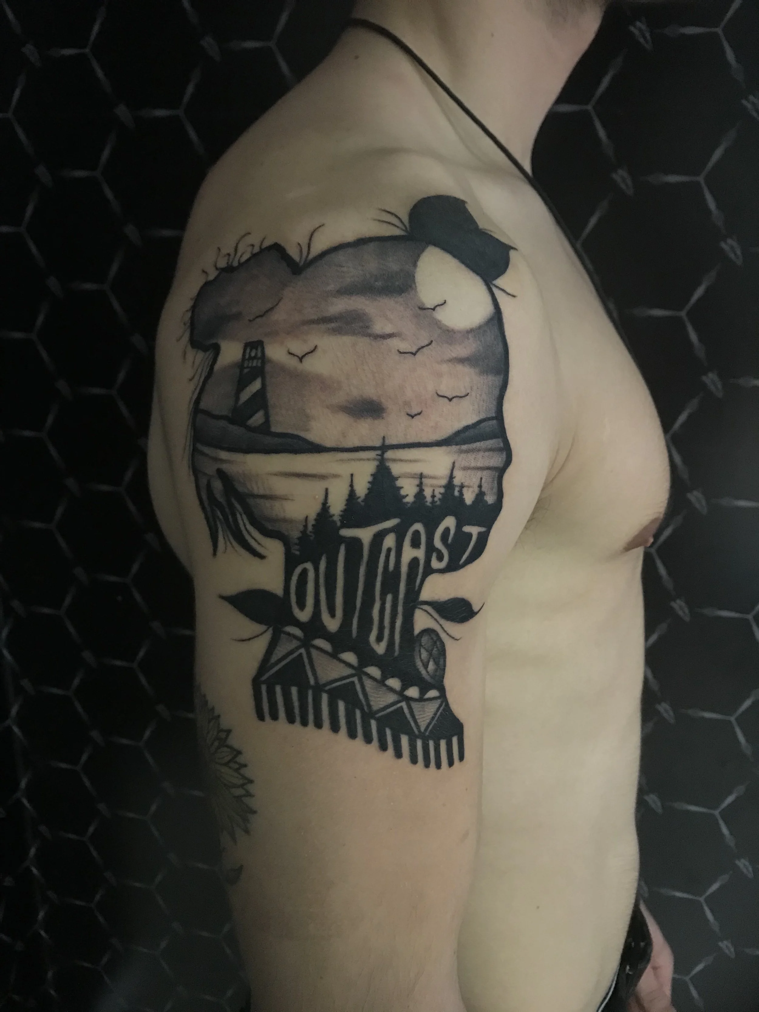 Tattoo on person's upper arm featuring a scenic landscape with a lighthouse, a full moon, birds in flight,istate trees, and the word OUTCAST with a wristwatch below.
