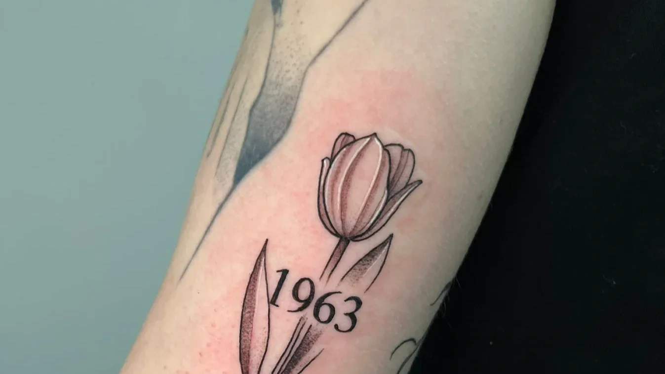 Tattoo of a tulip flower with the year 1963 underneath on a person's arm.