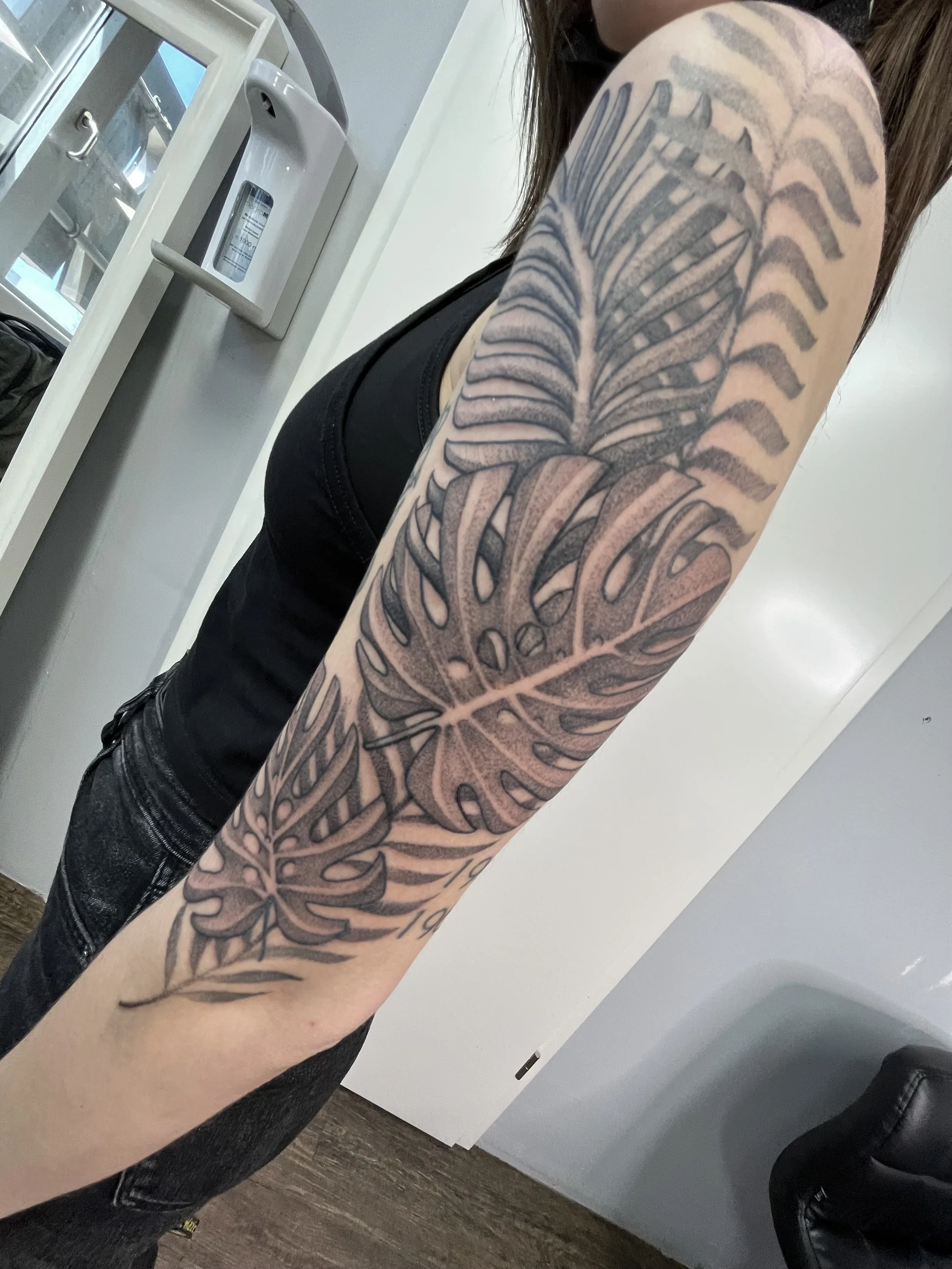 Tattoo of large tropical leaves on a person's arm.