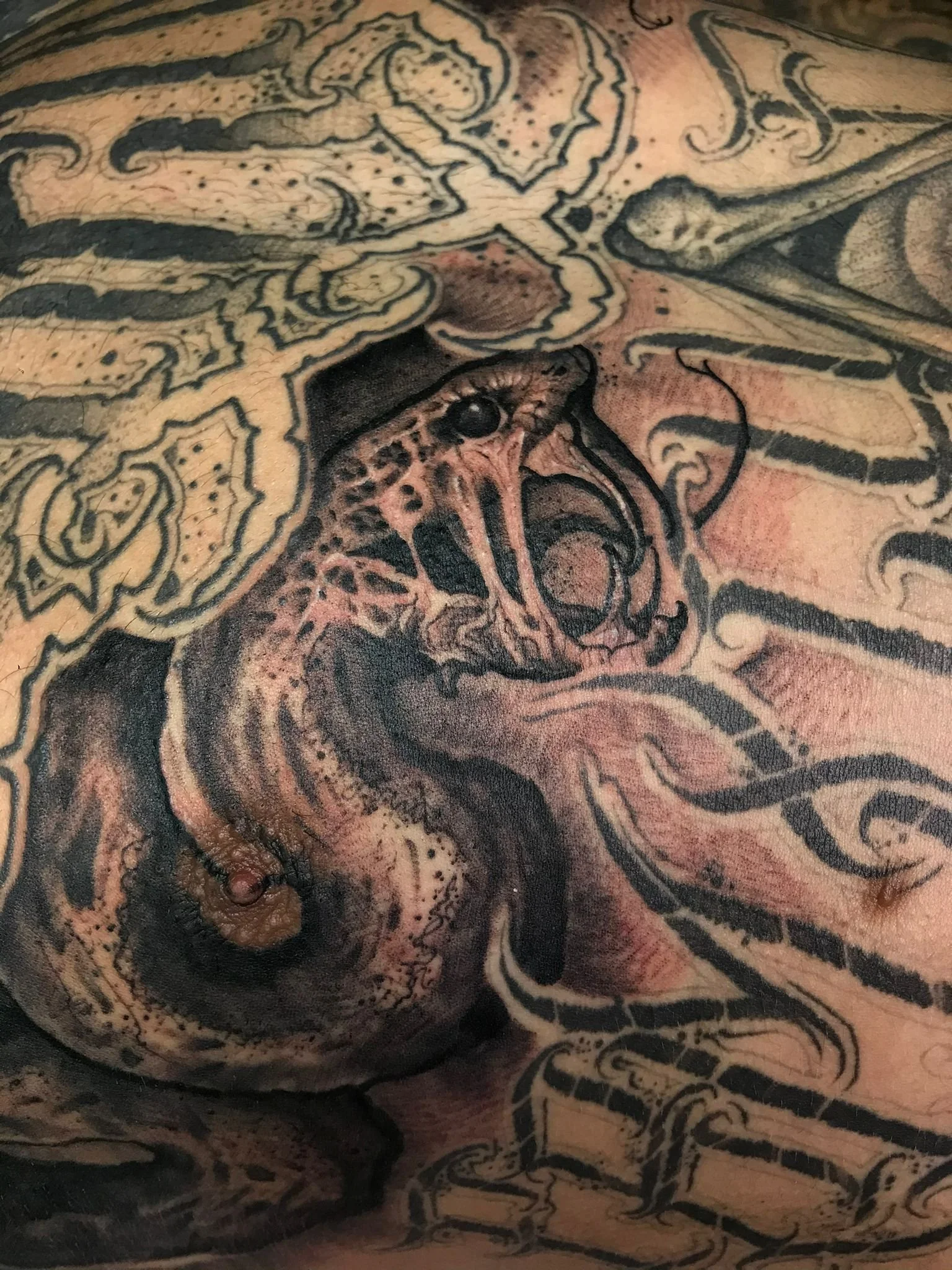 Close-up of a detailed tattoo featuring a colorful dragon intertwined with black and gray abstract and tribal designs.
