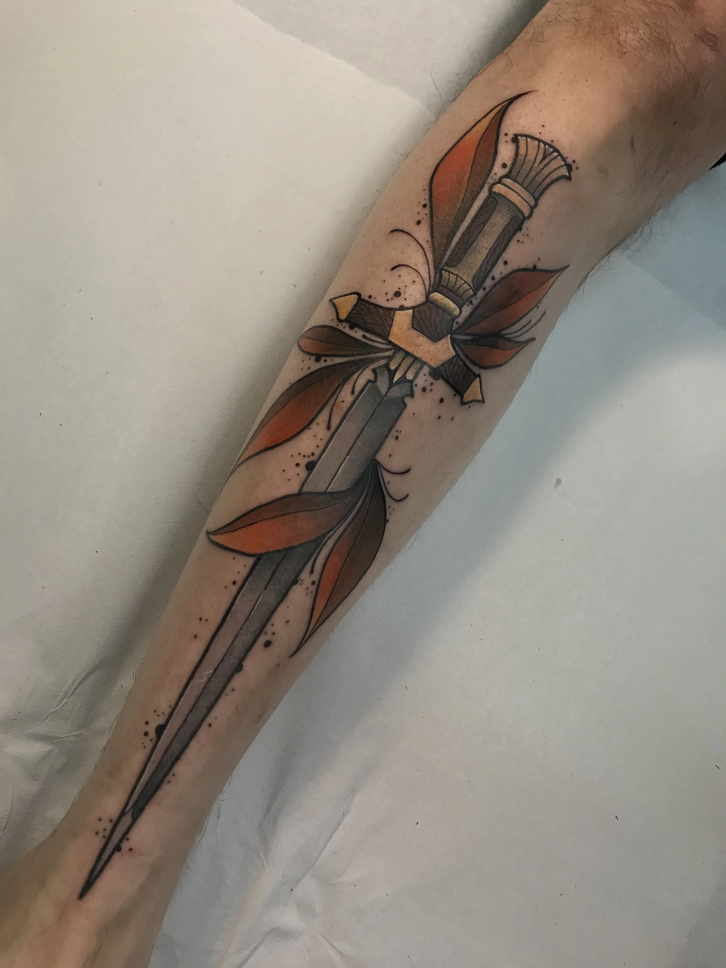 Tattoo of a dagger with leaves on the forearm.