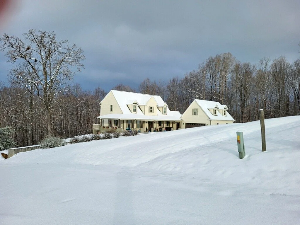 White house on a snow-covered hill with trees in the background and a dark cloudy sky.