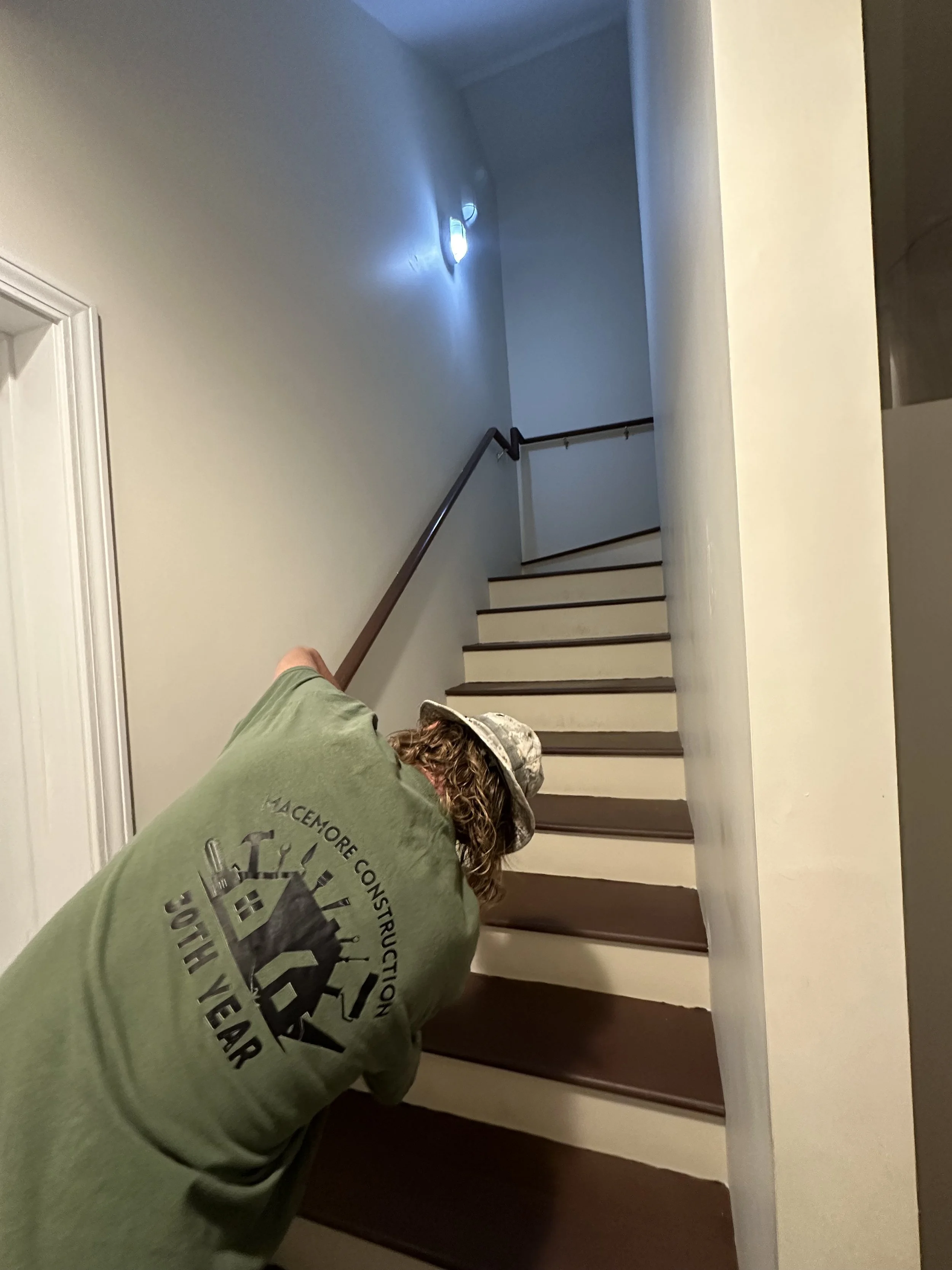 Person painting the edge of a stair step brown in a house interior.