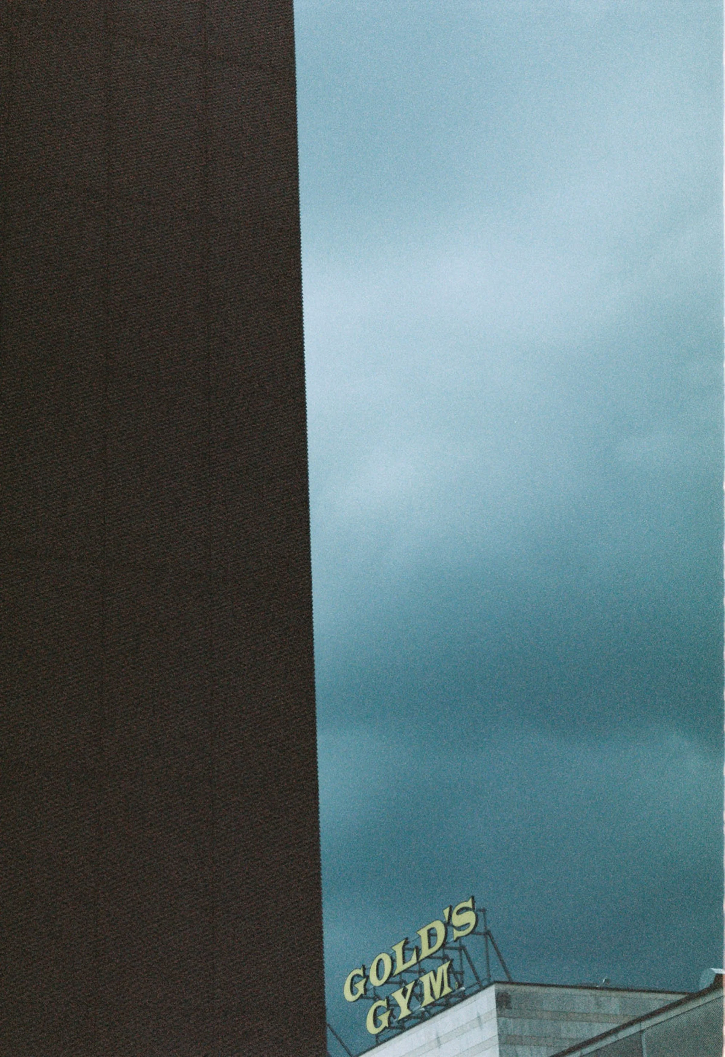 Dark brown building on the left, blue cloudy sky in the background, and a yellow sign at the bottom right corner that reads "GOLD'S GYM."