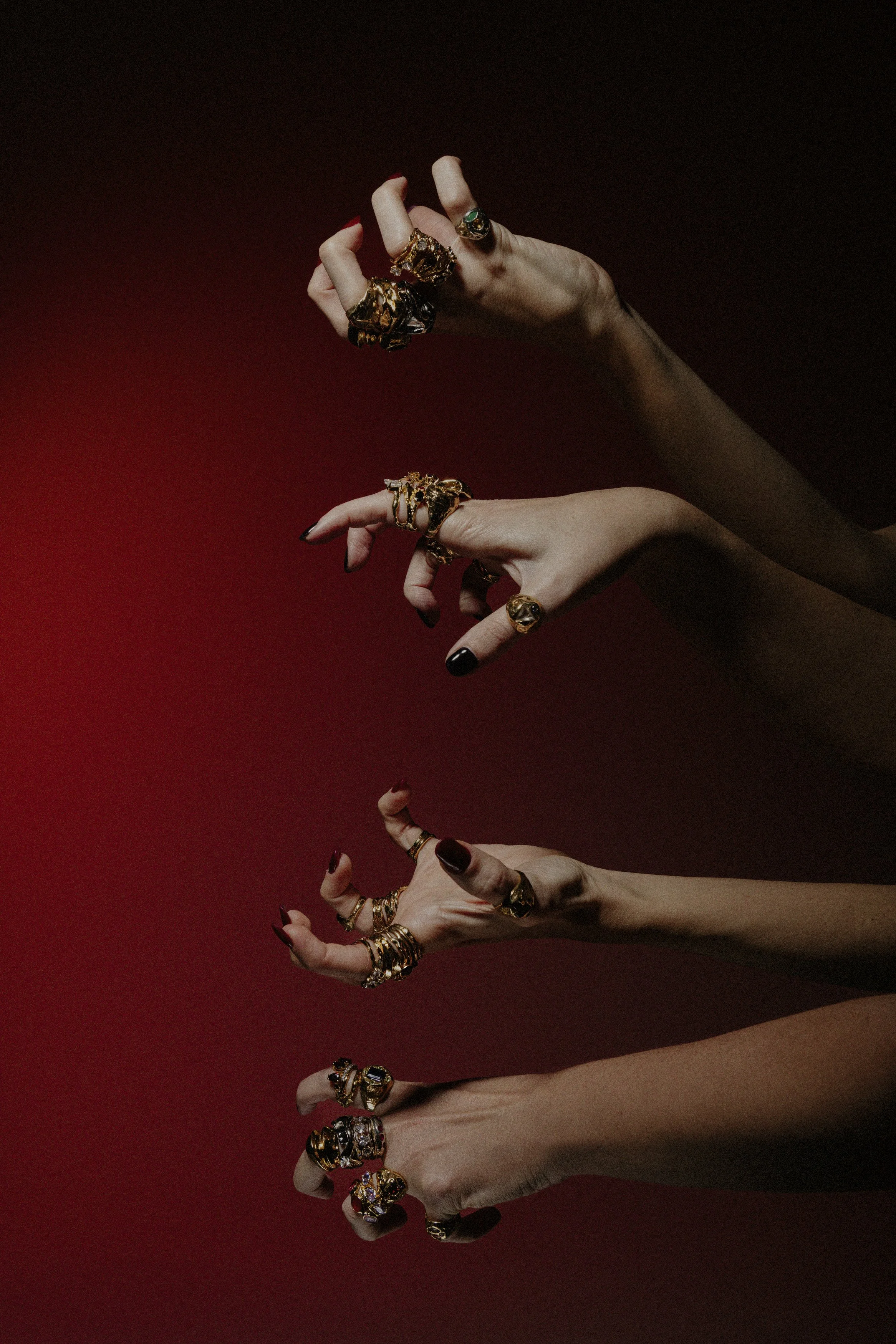 Multiple hands adorned with gold jewelry and rings, positioned against a red and black background.