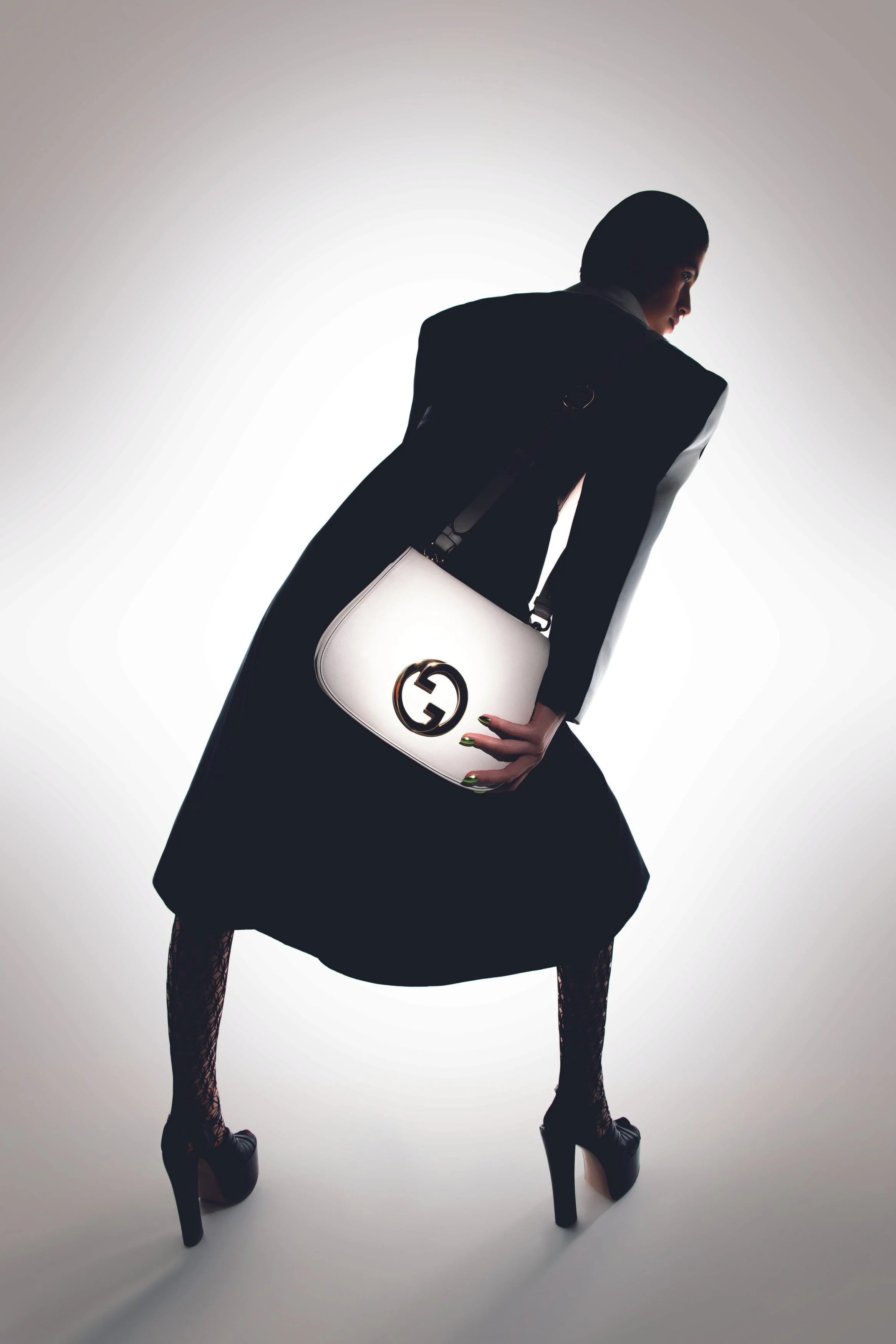 A fashion model dressed in black with high heels, carrying a white Gucci handbag with a gold logo, posing against a bright background.