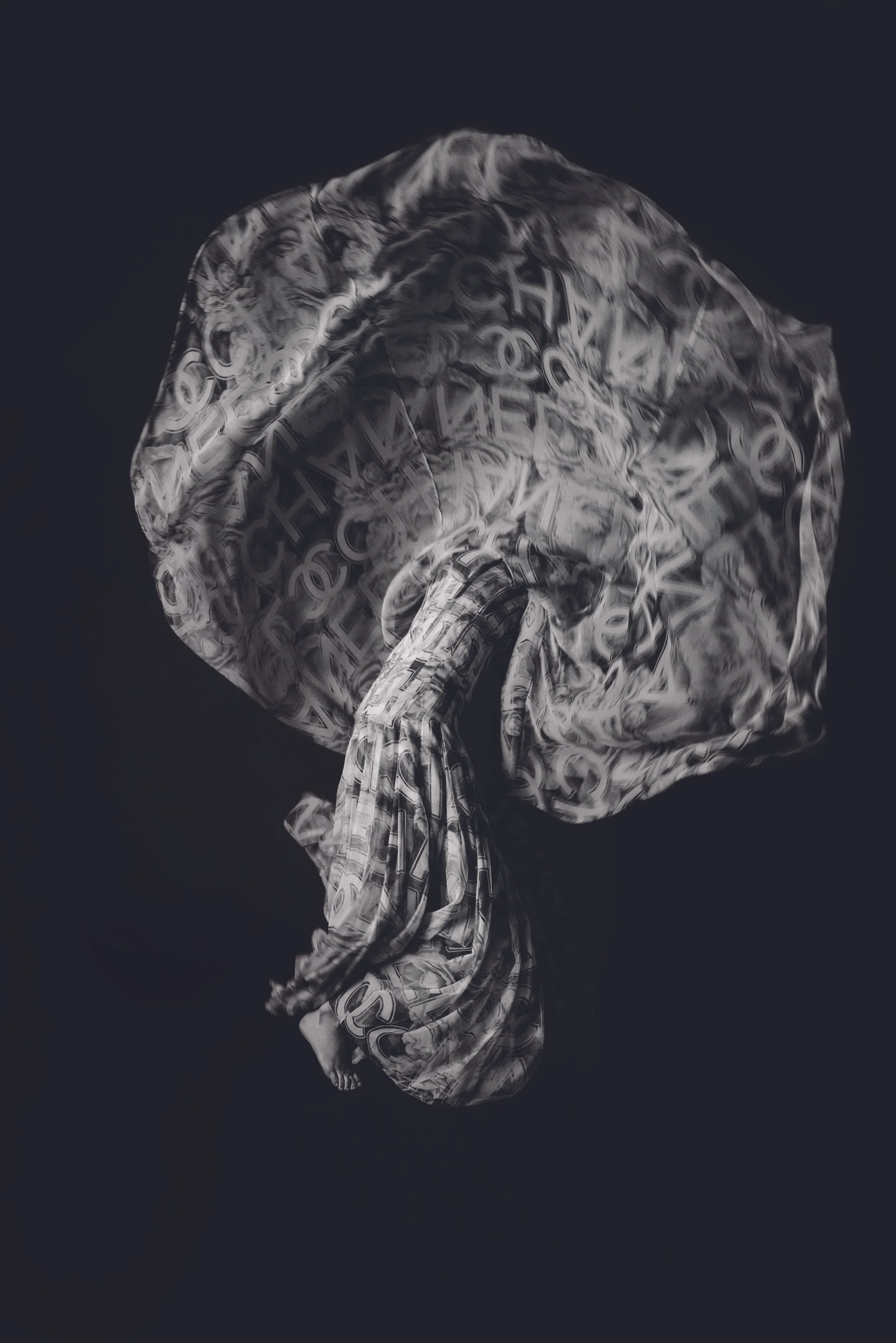 A person standing on their head with a large fabric wrapped around them, featuring black and white text and patterns, against a dark background.