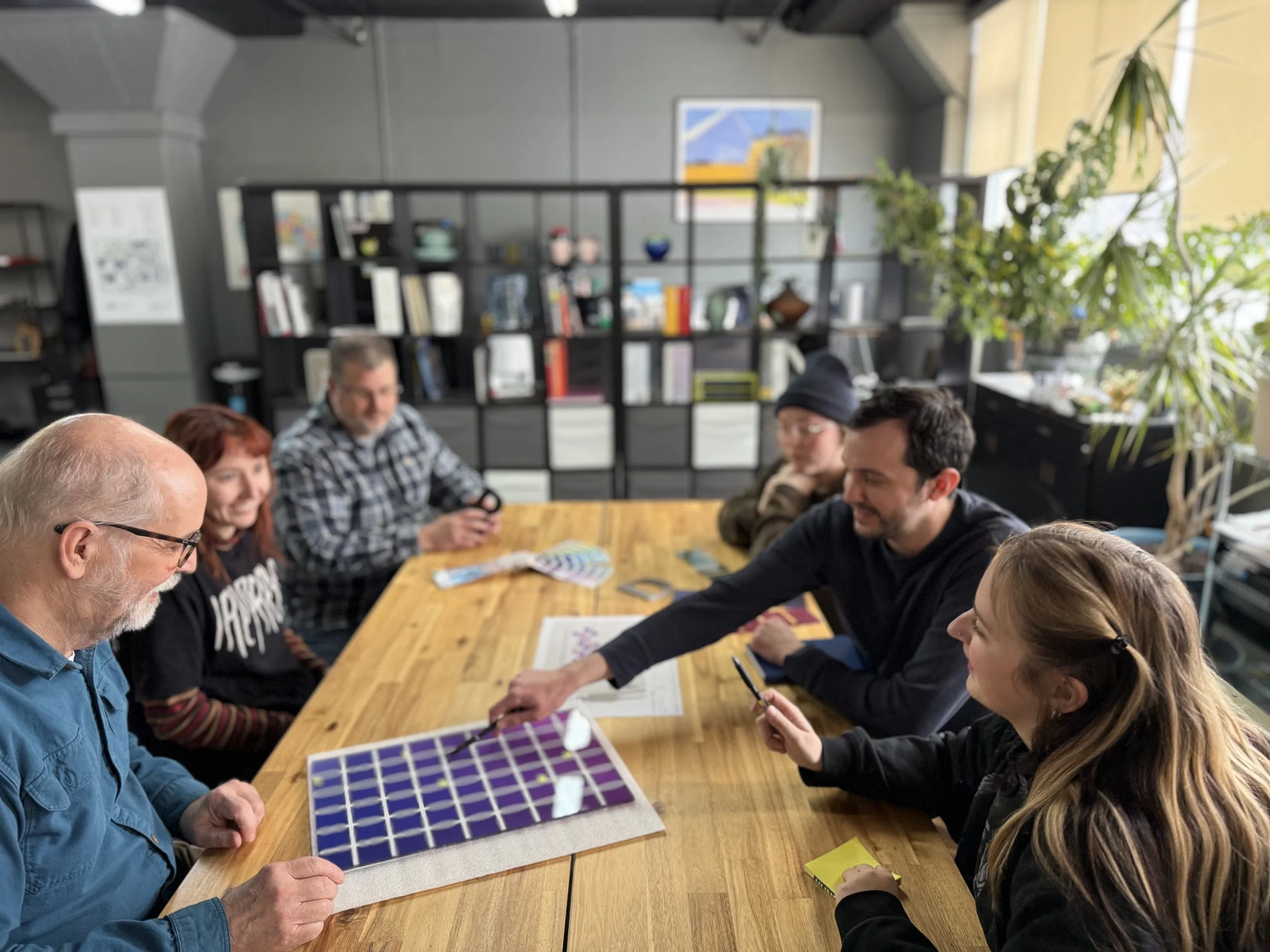 People gathered around a wooden table playing a board game in a cozy room with bookshelves, artwork, and plants.