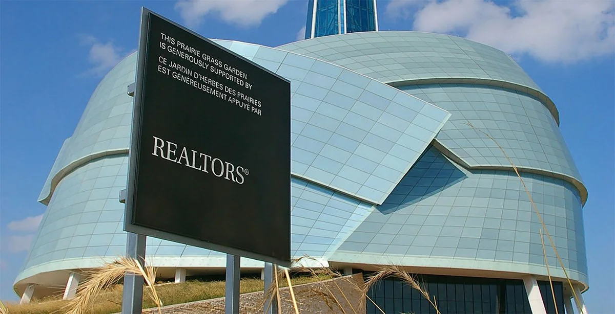 Modern glass building with a large sign in front that reads 'This prairie grass garden is generously supported by Realtors'.
