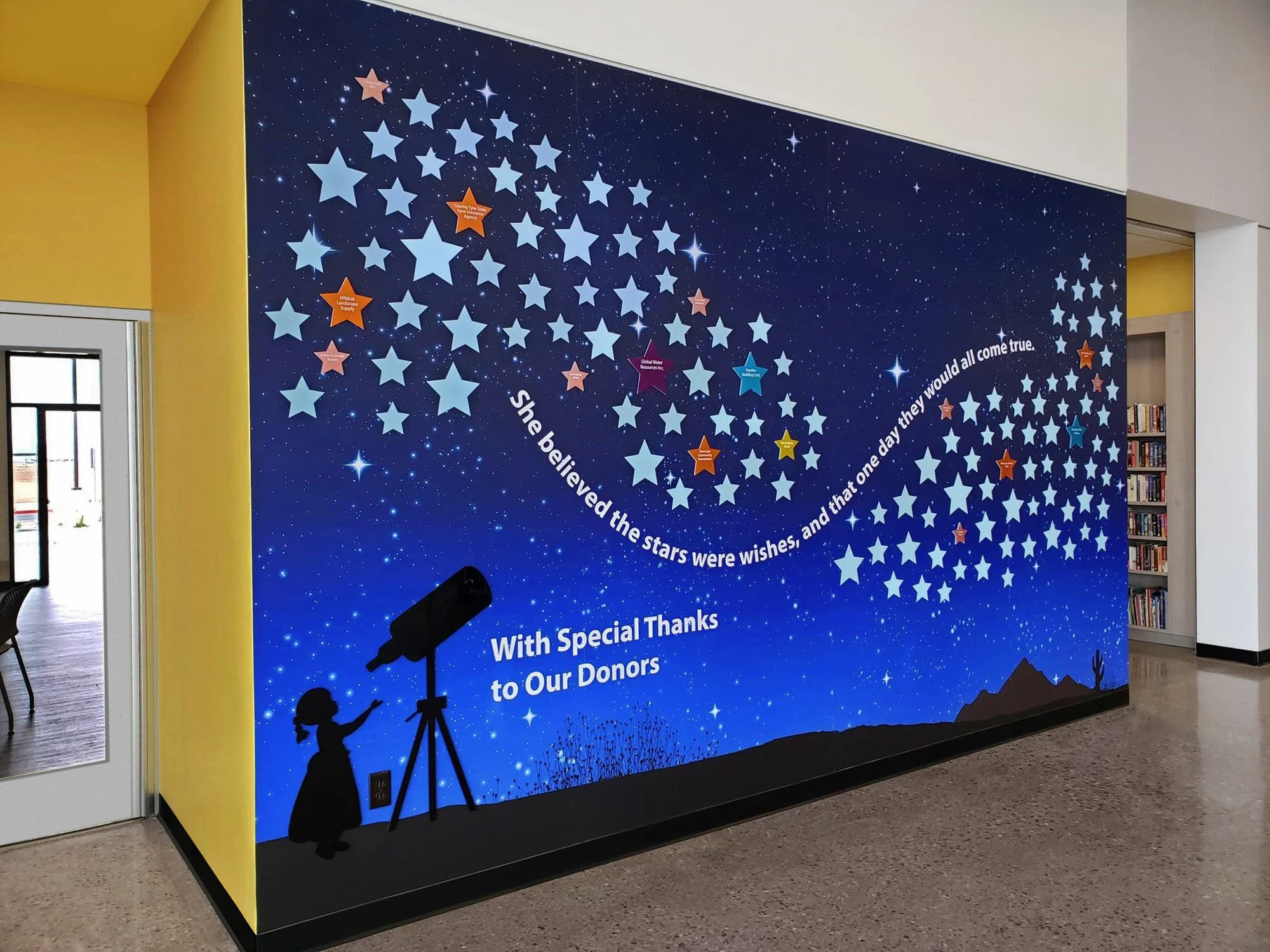 Night sky themed wall mural with stars, constellations, and a girl looking through a telescope, inscribed with a thank you message for donors.