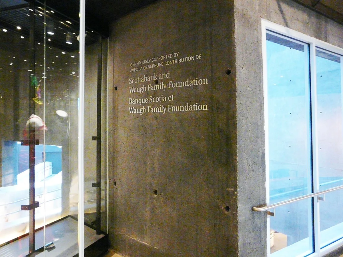 A concrete wall with text in both English and French, crediting support from Scotiabank and Waugh Family Foundation, next to a glass door entrance.