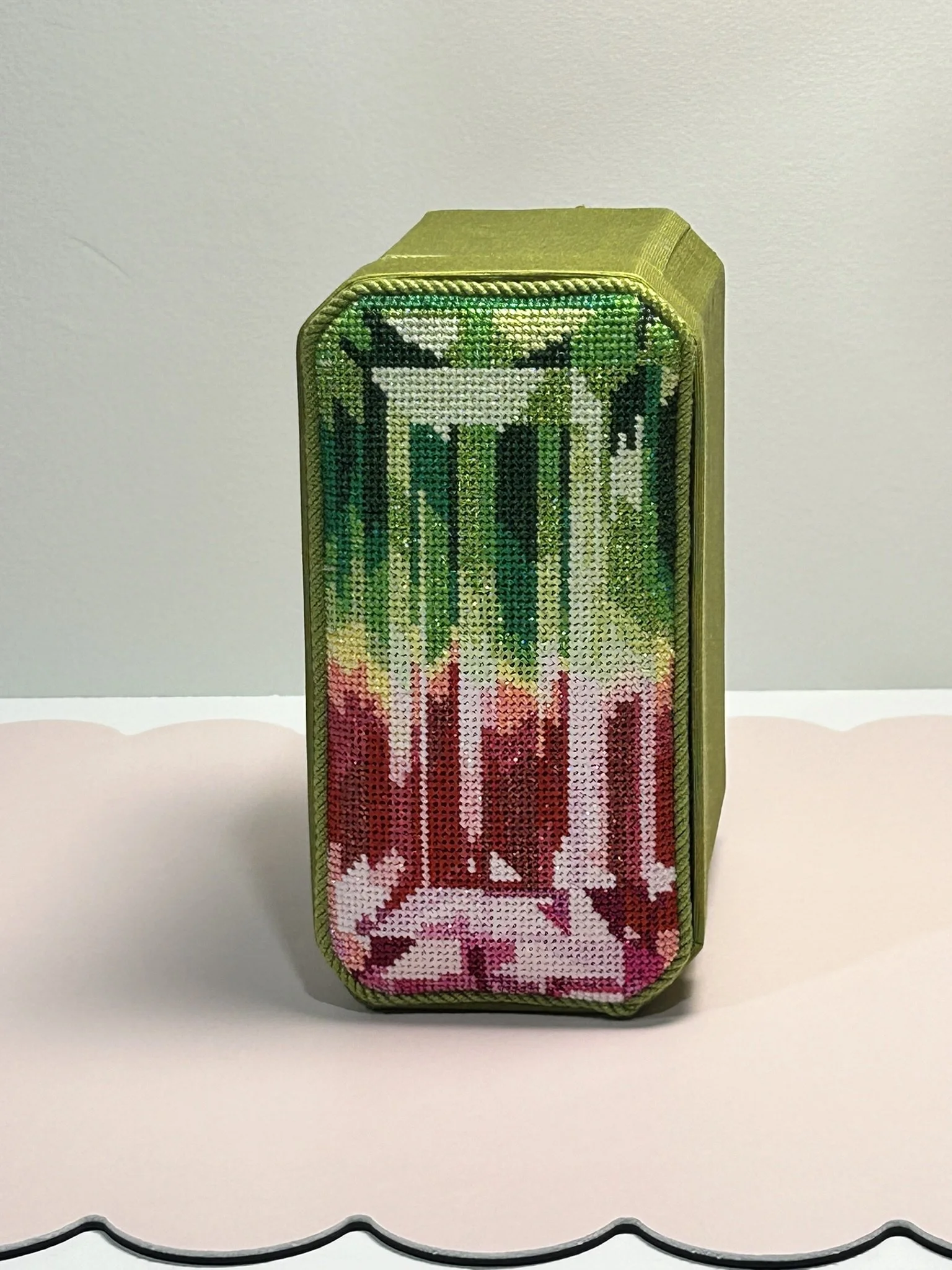 An oblong rectangular box with an intricate stitching to look like a cushion cut gem on top featuring shades of greens and pinks.