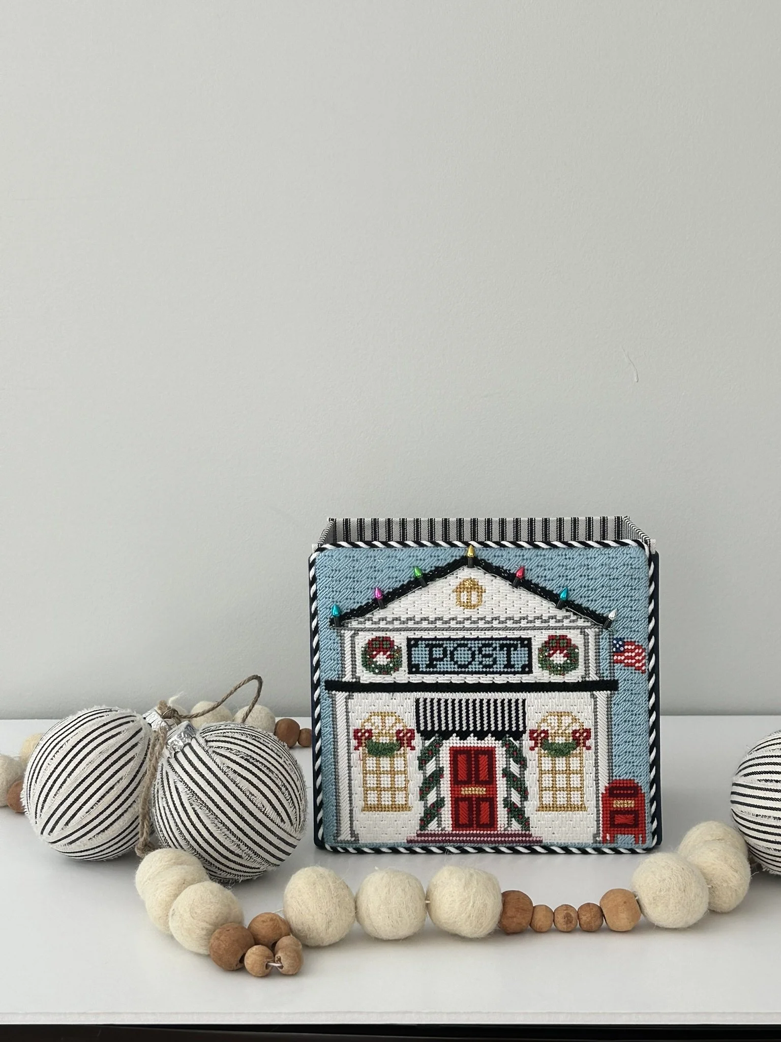 An open top box for holiday cards.  The needlepoint front is a post office decorated festively for the winter holidays.