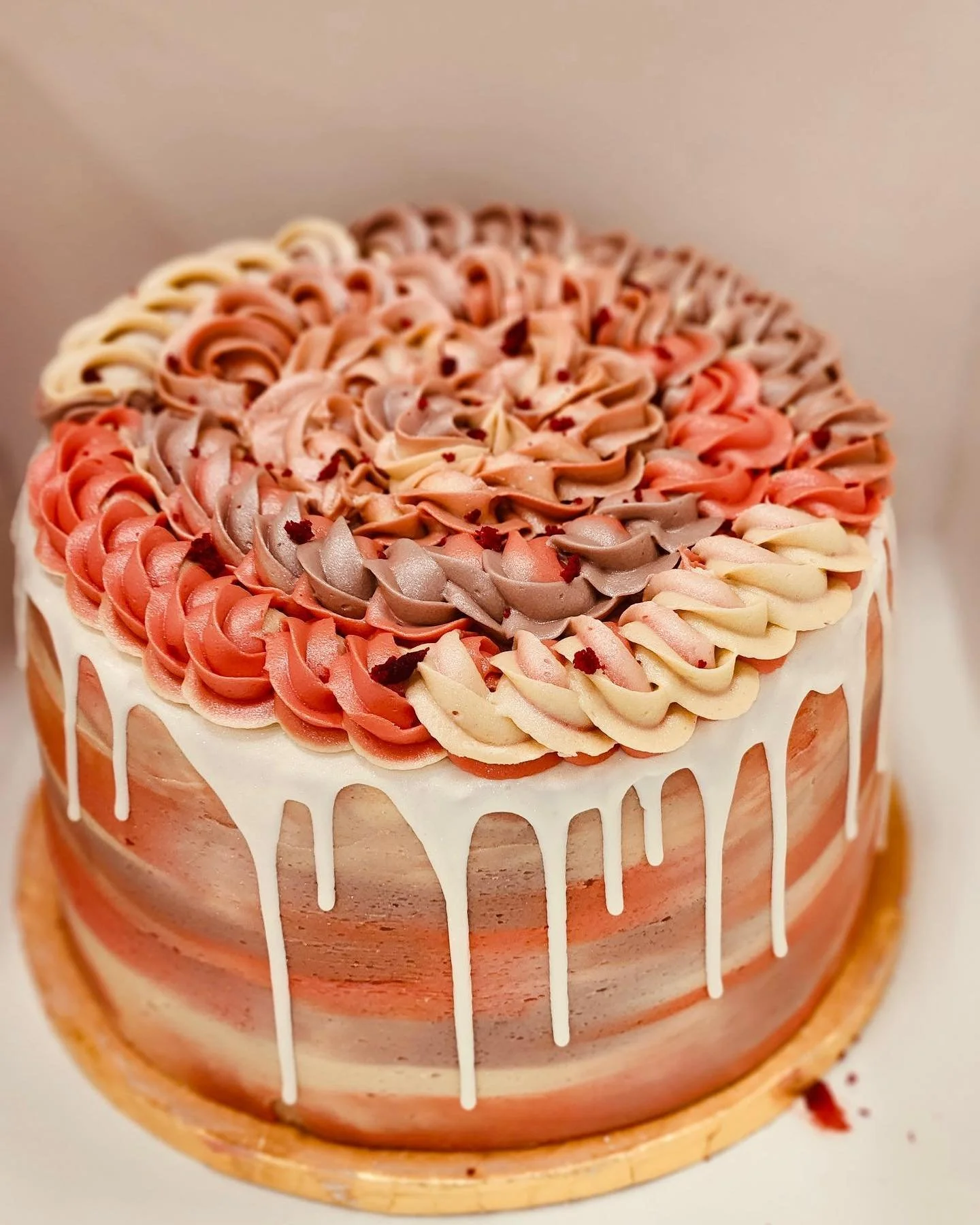 A round layered cake with orange, pink, and white frosting, topped with colorful buttercream swirls and white drip icing on the sides.