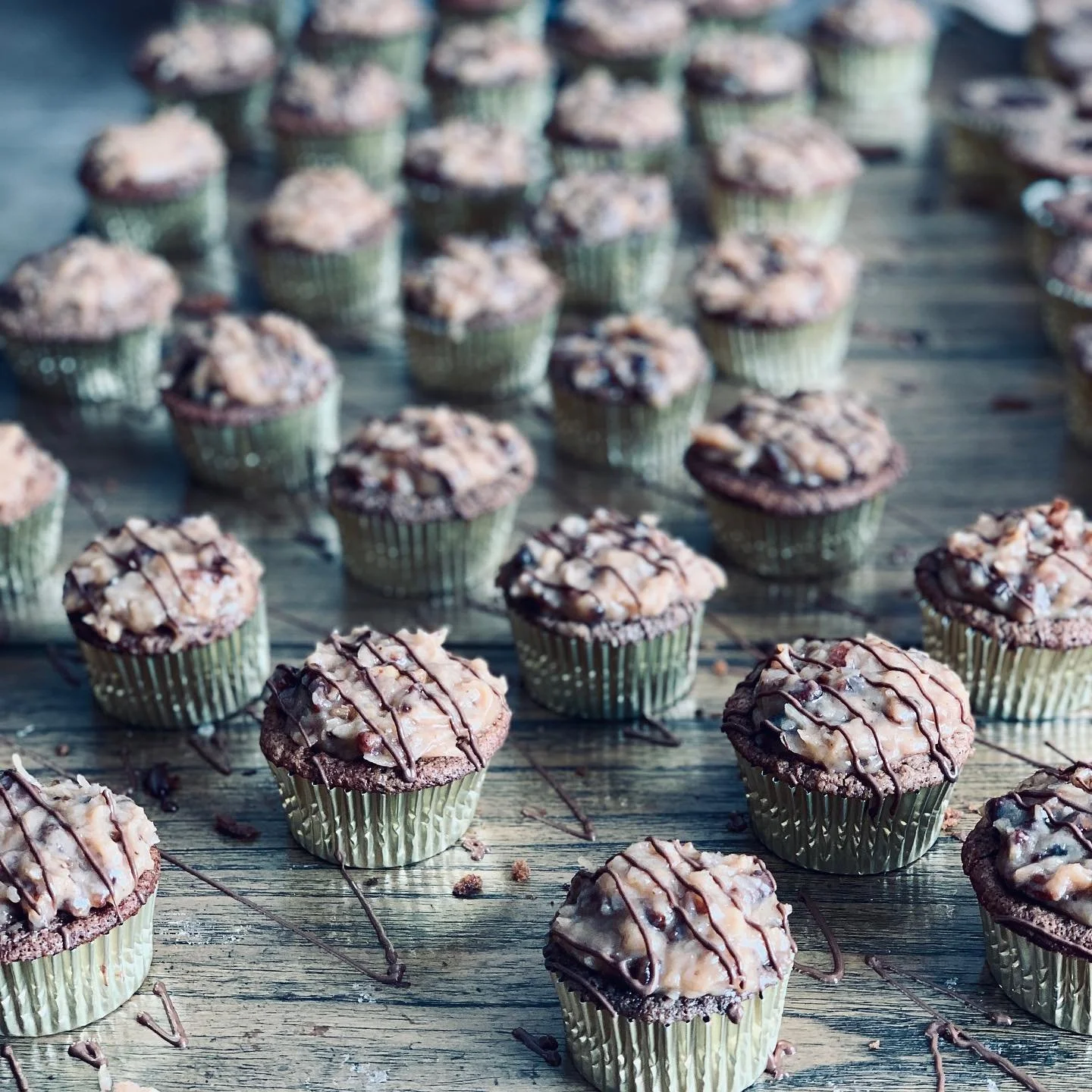 Multiple cupcakes with chocolate and frosting, decorated with chocolate drizzles, arranged on a rustic wooden surface.