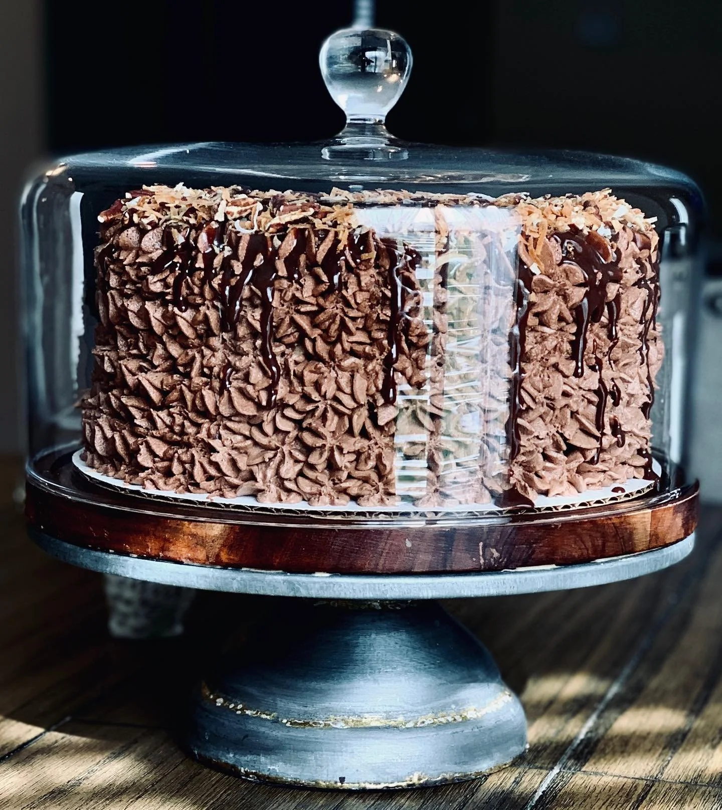 Chocolate cake with piped frosting and chocolate drizzle on a glass cake stand with a wooden base.