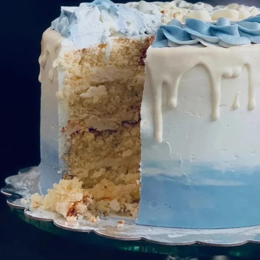 A partially sliced birthday cake with white and blue icing and decorations.
